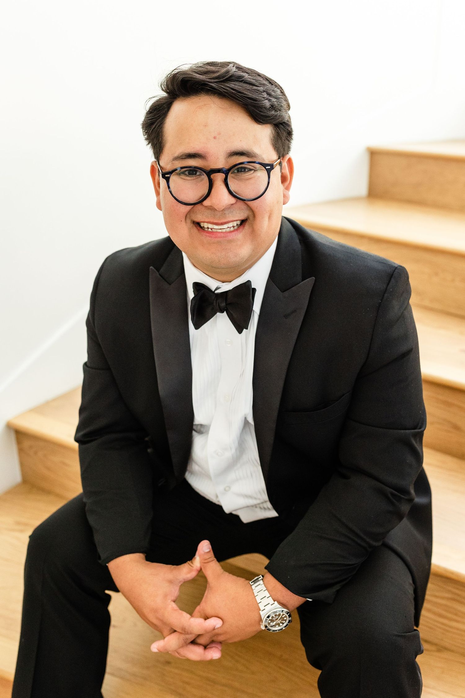 Smiling man in black tuxedo and bow tie sitting on wooden stairs. tampa wedding