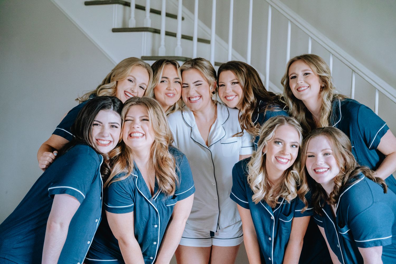 Group of bridesmaids in matching navy pajamas smiling together on stairs.