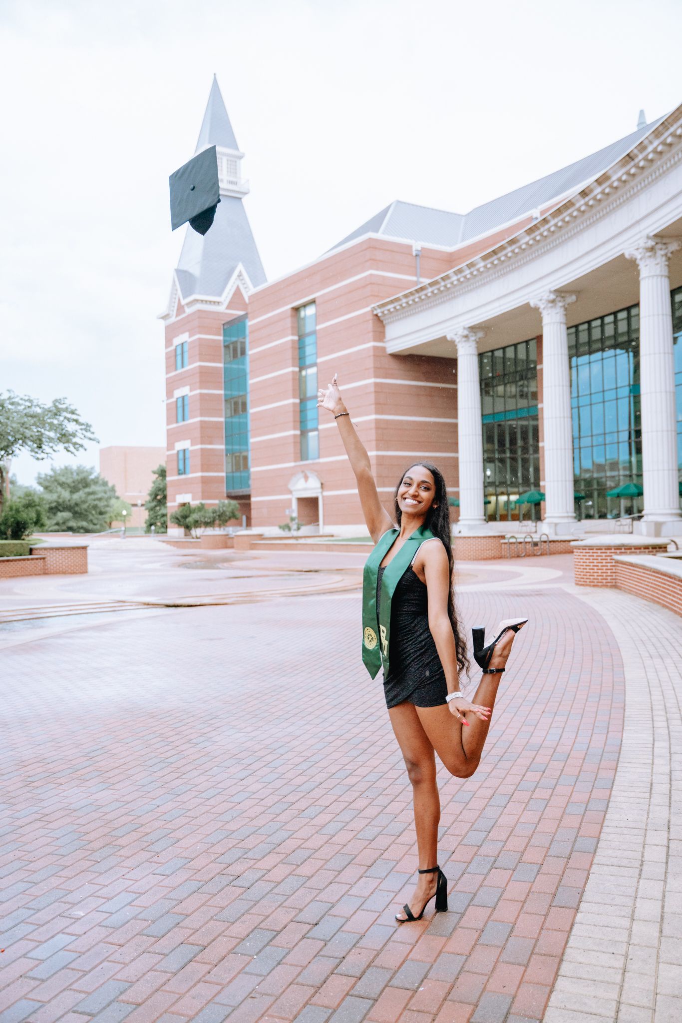 Graduate tossing cap in air while posing in front of a brick university building.