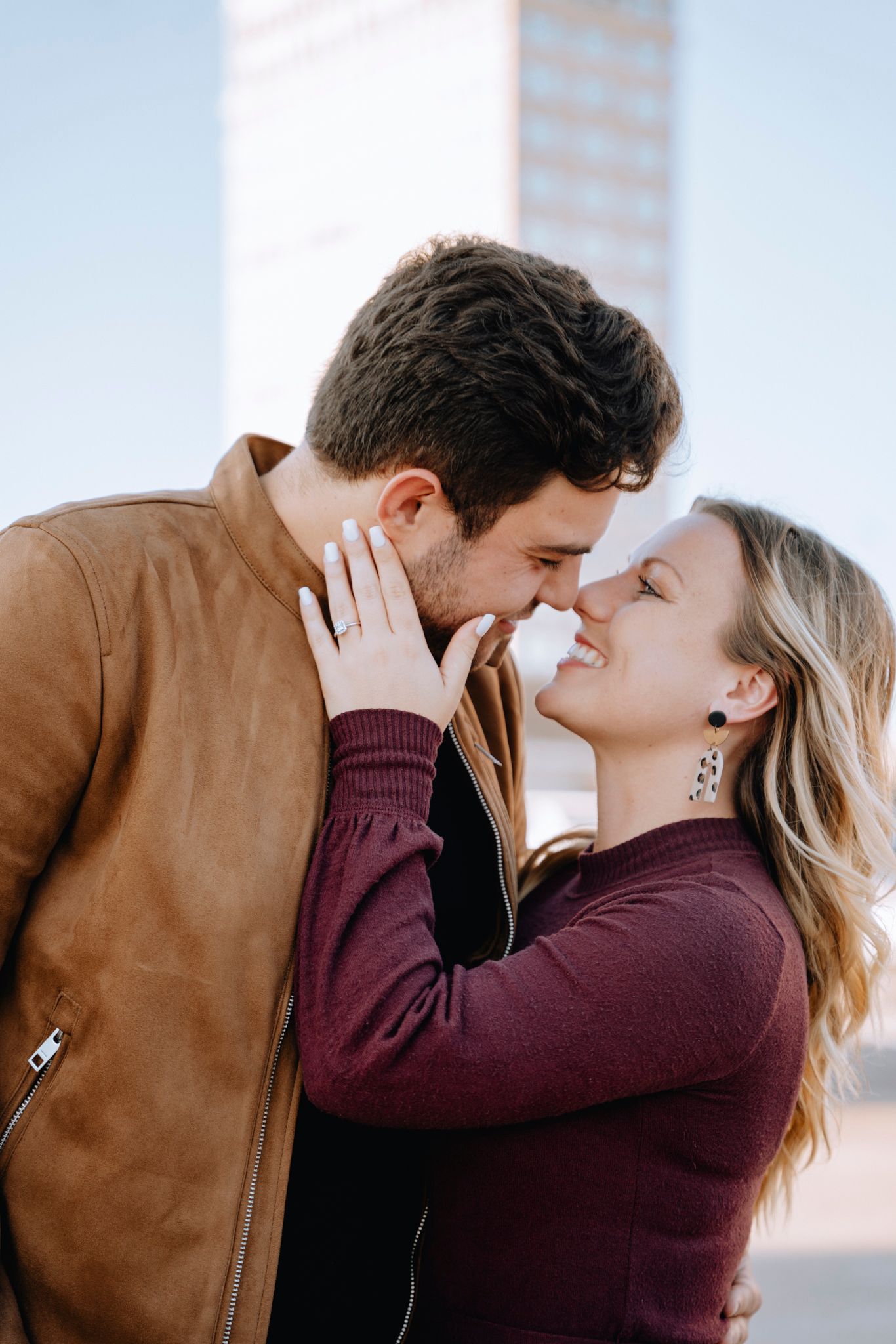 Couple sharing a romantic nose-to-nose moment, woman in burgundy dress holding mans face tenderly.