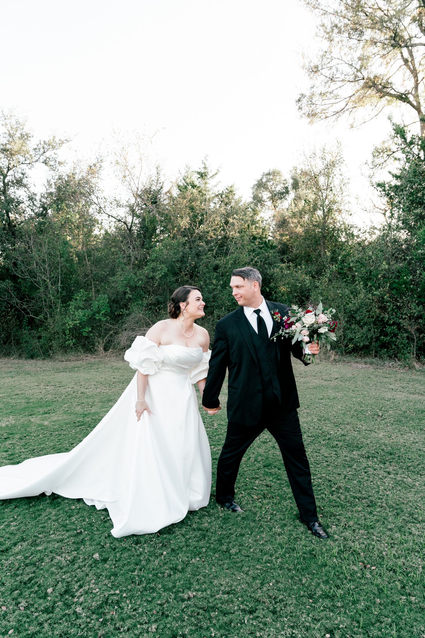 Bride and groom walking hand in hand on green lawn at sunset.