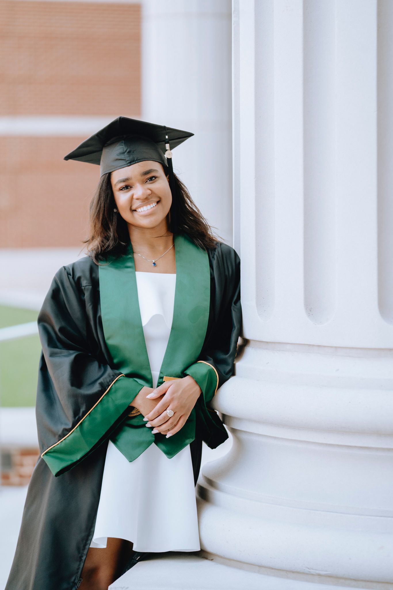 Female Baylor University graduate in black cap and gown with green stole poses by white columns.