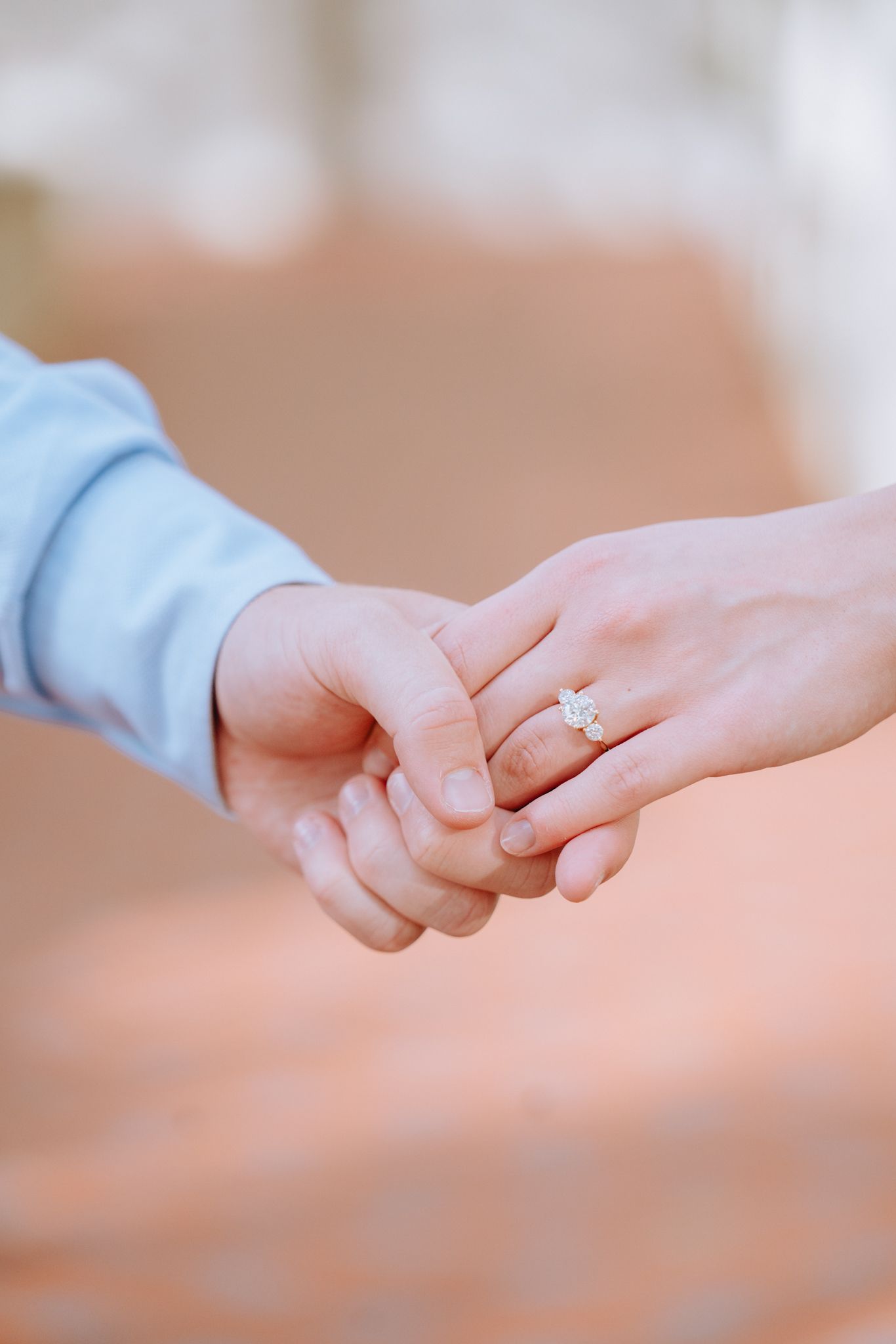Close-up of couple holding hands showing elegant diamond engagement ring on woman's finger.