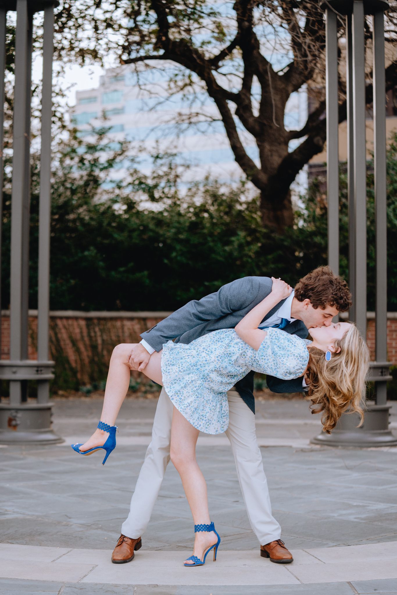 Couple sharing romantic dip kiss outdoors with city backdrop.