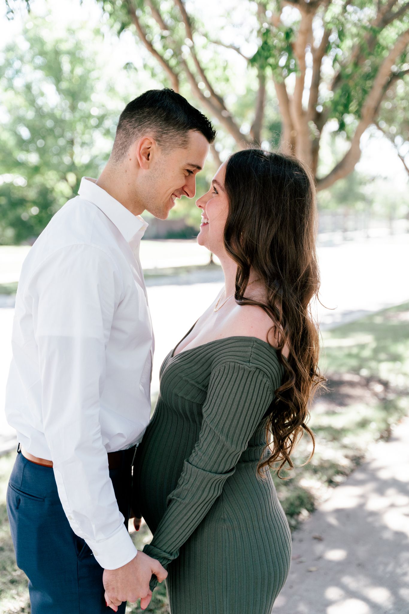 Couple touching foreheads tenderly in sunny park setting.