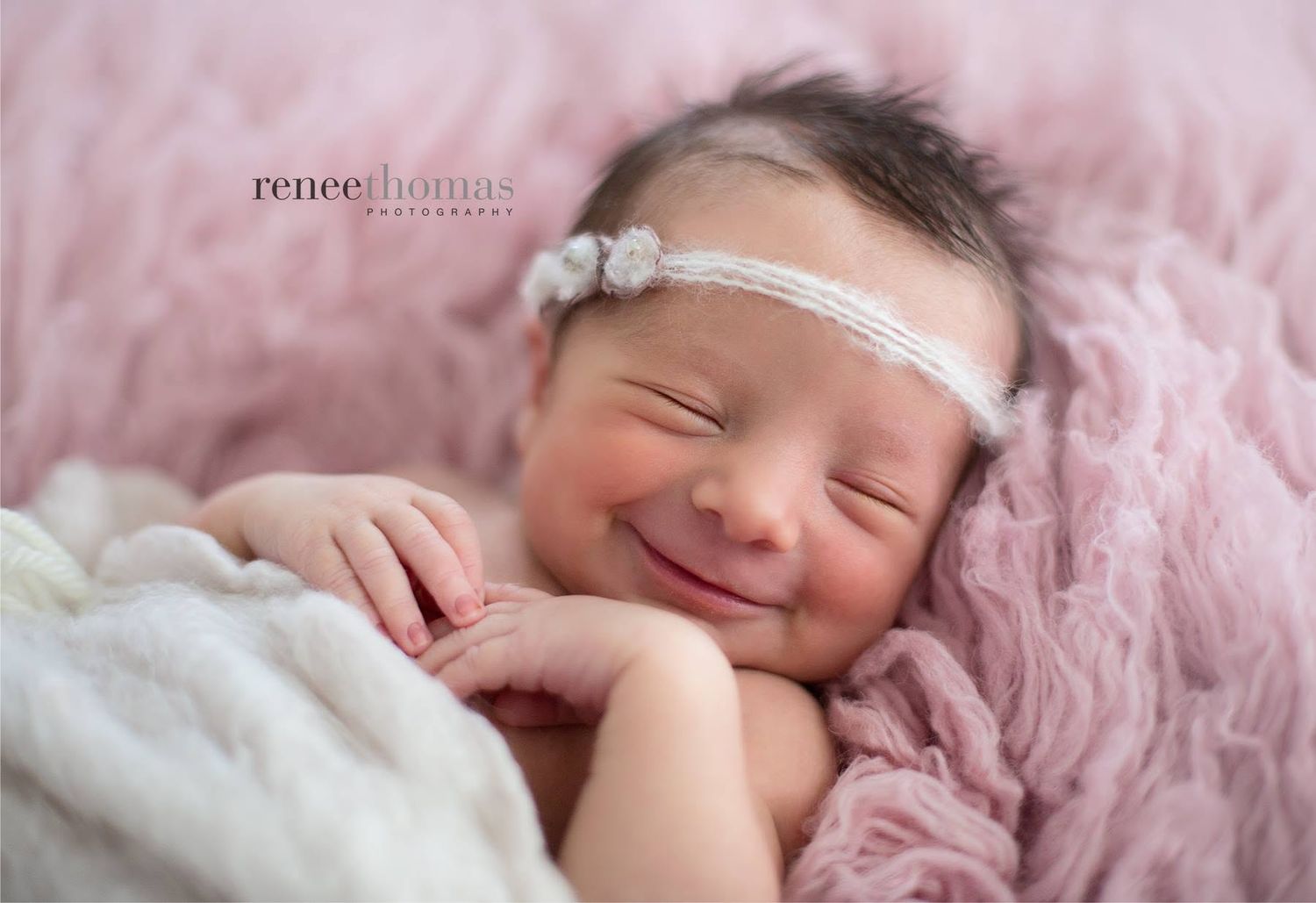 Smiling newborn baby girl with floral headband on pink backdrop by Renee Thomas Photography.