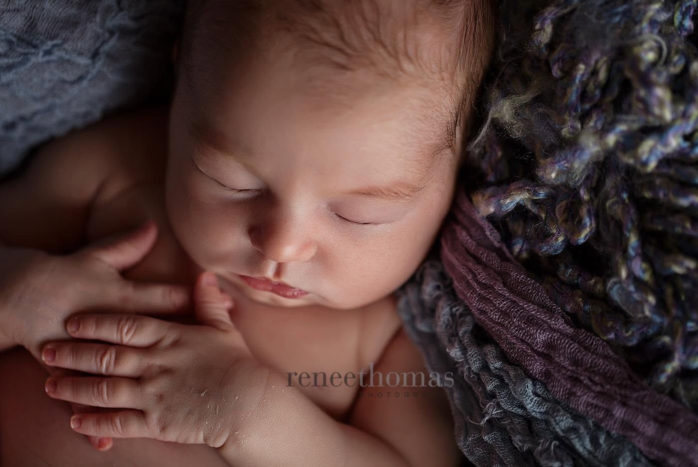 Close-up of peaceful sleeping newborn baby wrapped in soft purple textured blanket.