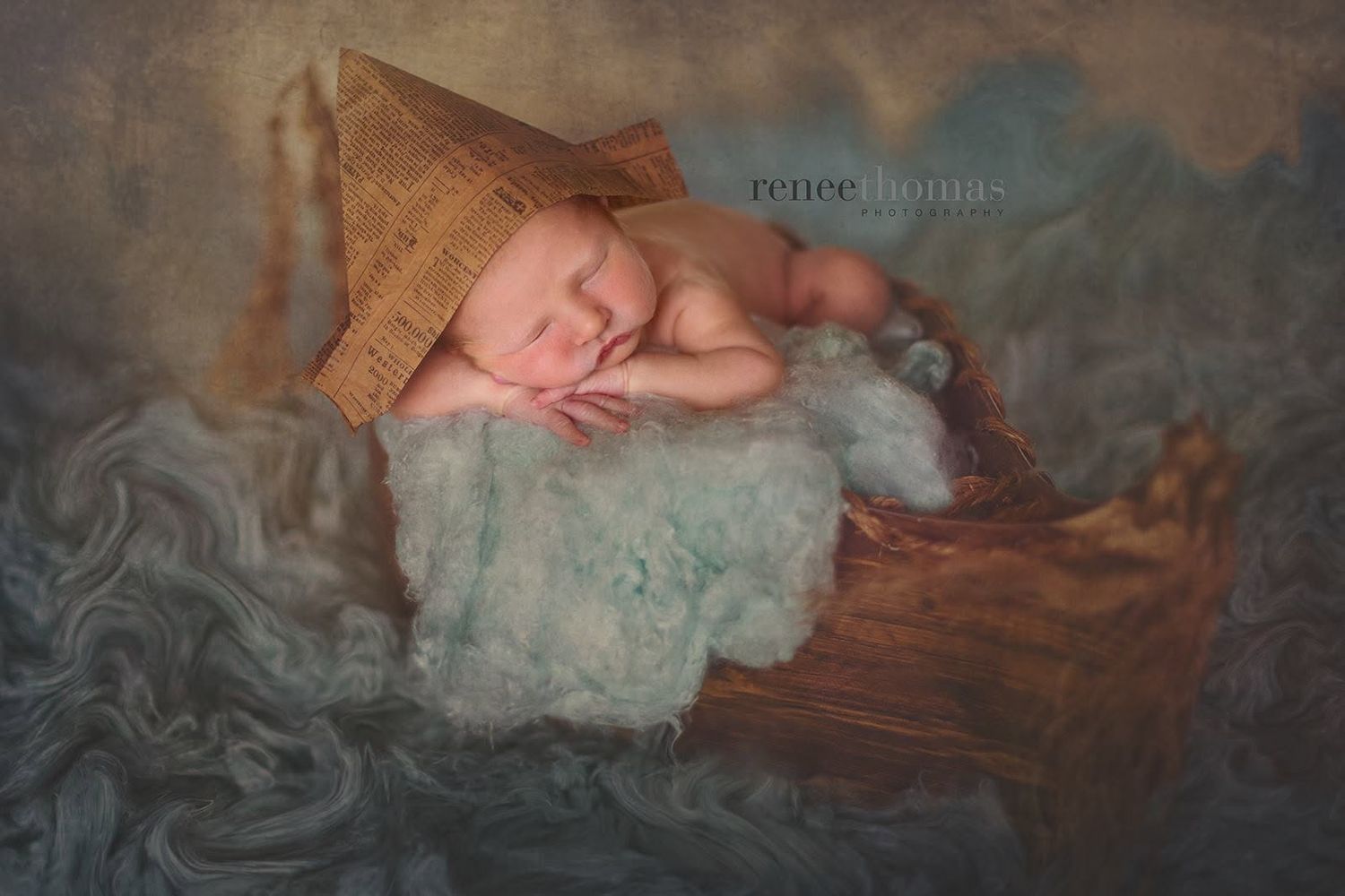 Sleeping newborn baby wearing a brown knit hat posed in a wooden boat prop with blue fluffy wrap.
