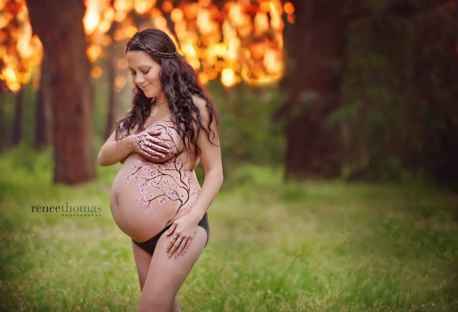Pregnant woman with belly art posing outdoors in golden sunset forest light.