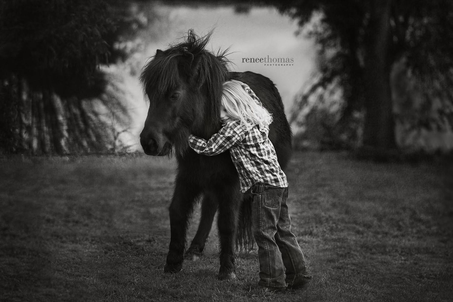 Black and white photo of a young child hugging a small pony in a grassy field.