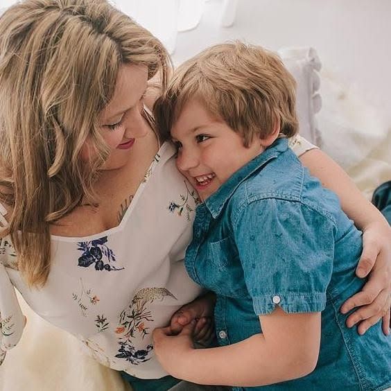 A smiling mother and young boy share a joyful cuddle together in a bright, airy indoor setting.