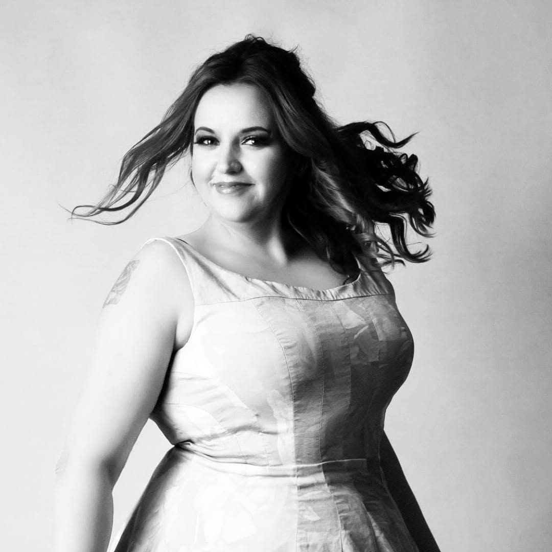 Black and white portrait of a smiling plus-size woman in a white dress with flowing hair.