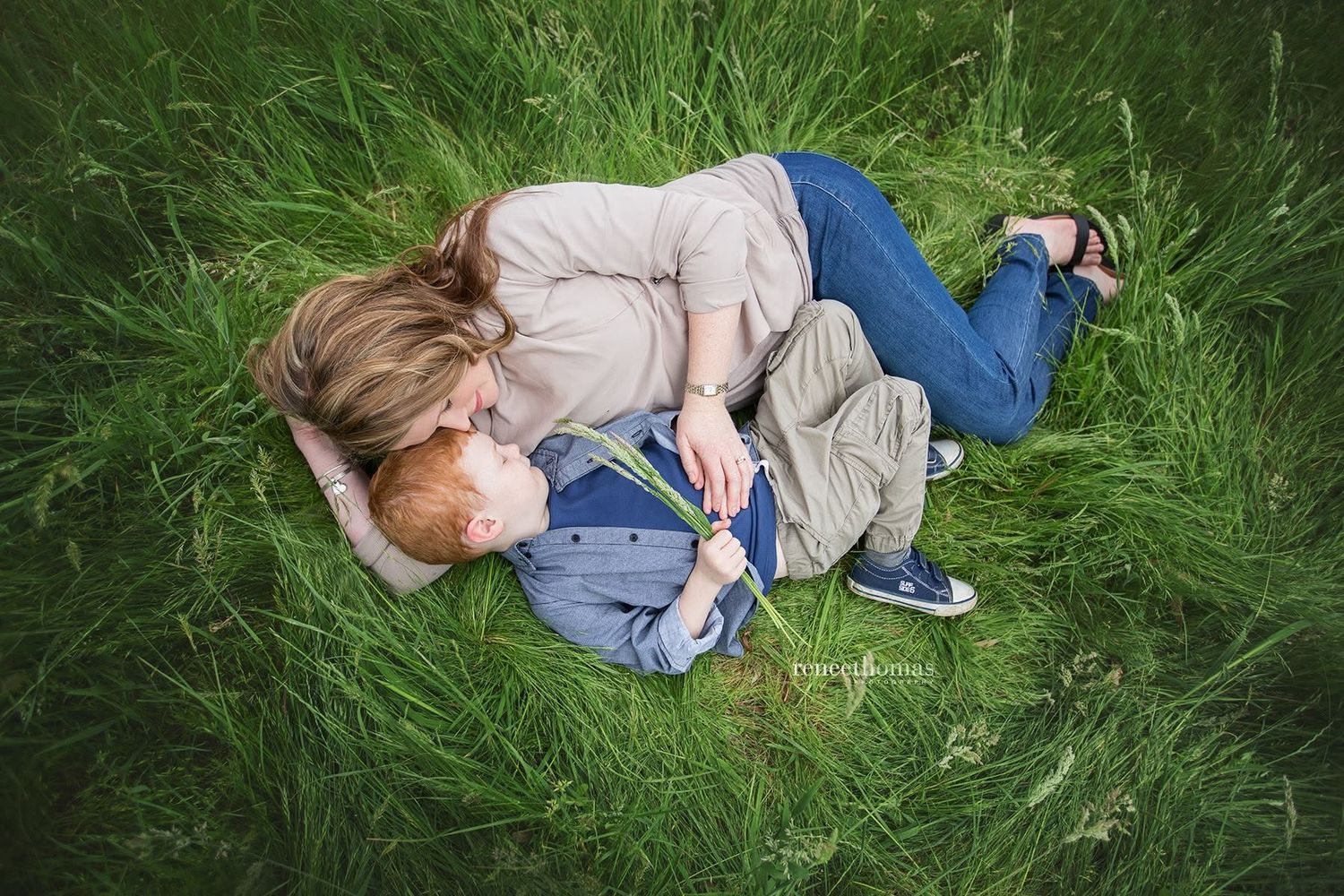 Mother and young child lying together in lush green grass sharing a tender moment.