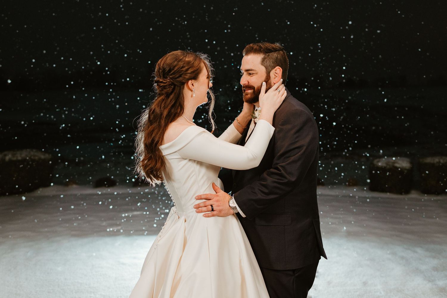 A romantic winter wedding photo with snow falling as couple dances in formal attire.