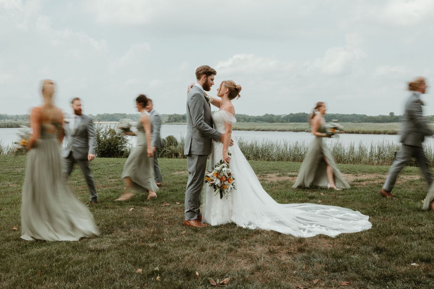 Wedding couple poses in field while wedding party creates motion blur effect around them.