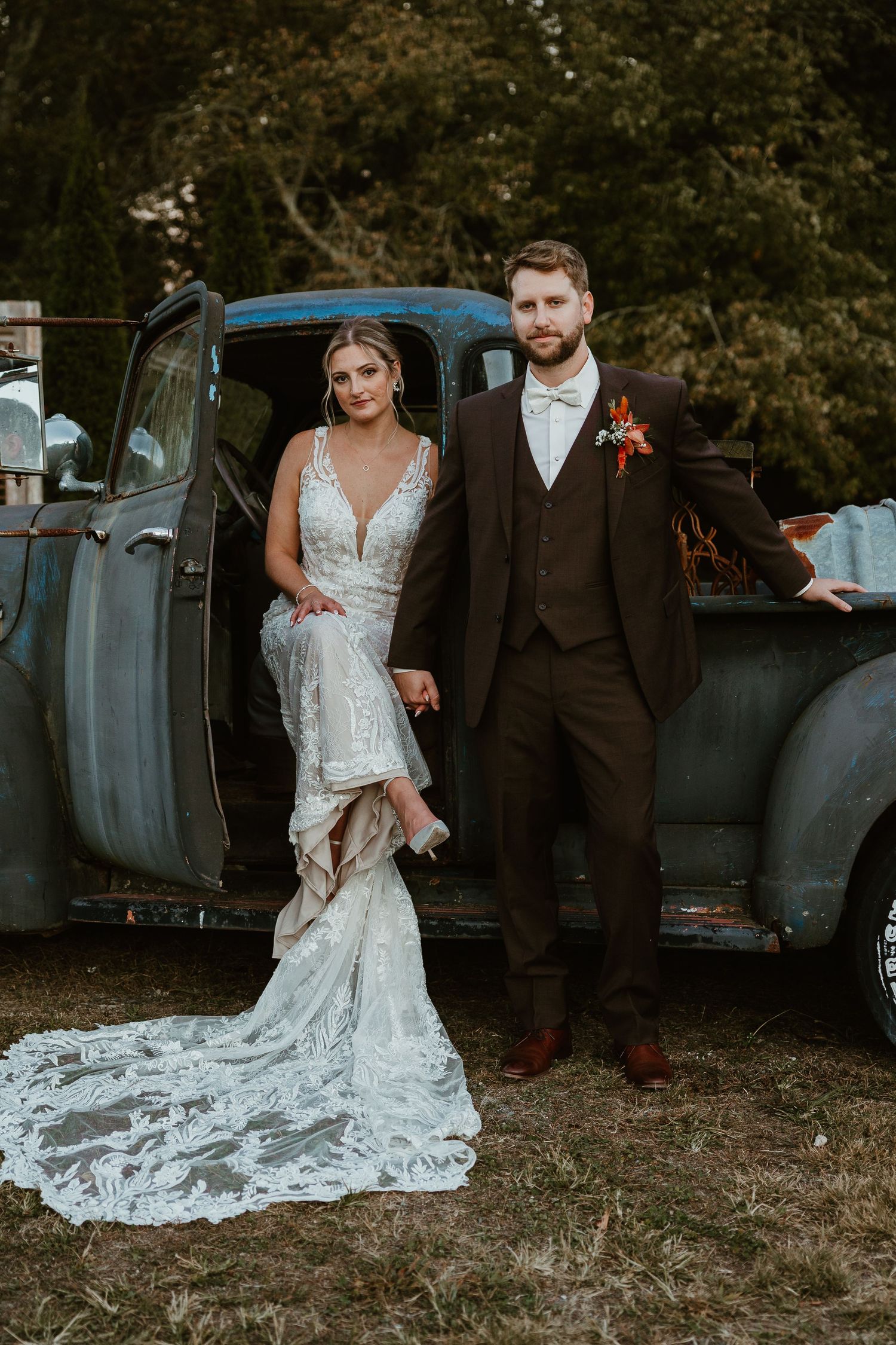 Newlyweds pose by vintage blue truck, bride wearing lace gown with dramatic train.