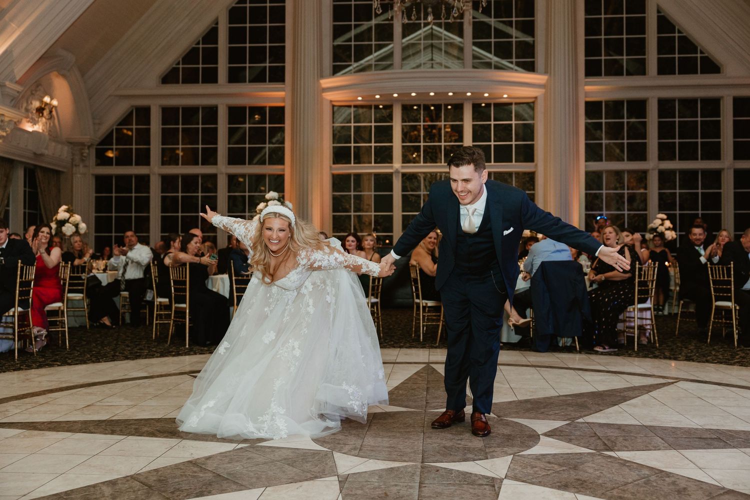 Couple dances energetically in elegant reception hall with vaulted ceiling and chandelier.