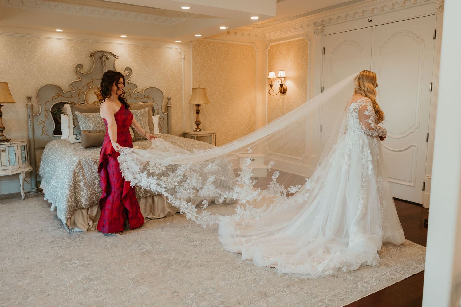 A flowing cathedral length lace veil trails behind an elegant white wedding gown in an ornate dressing room.