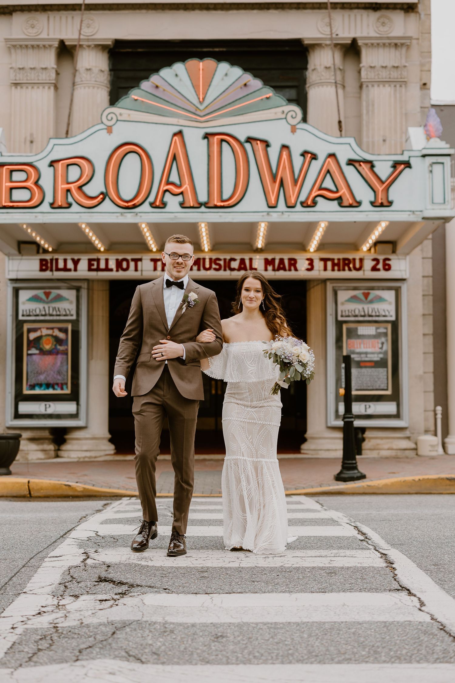 Wedding couple poses in front of vintage Broadway theater marquee displaying Billy Elliot musical.