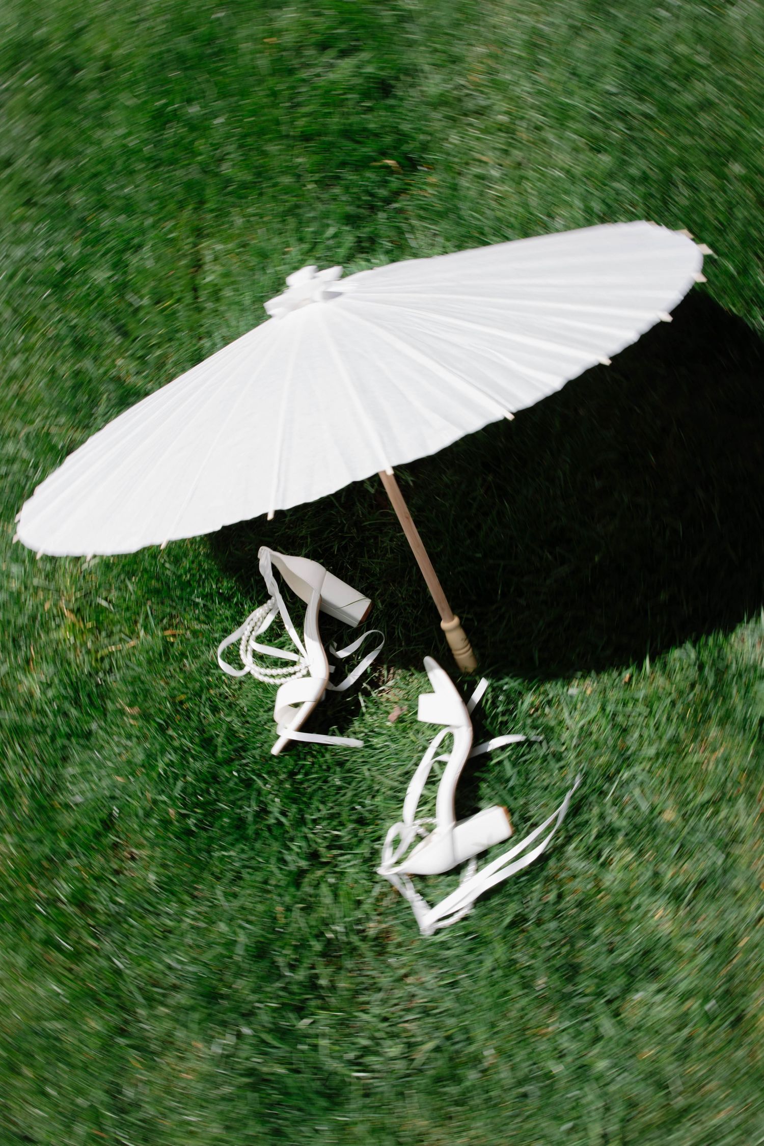 White paper parasol and elegant white lace-up shoes arranged on green grass outdoors.