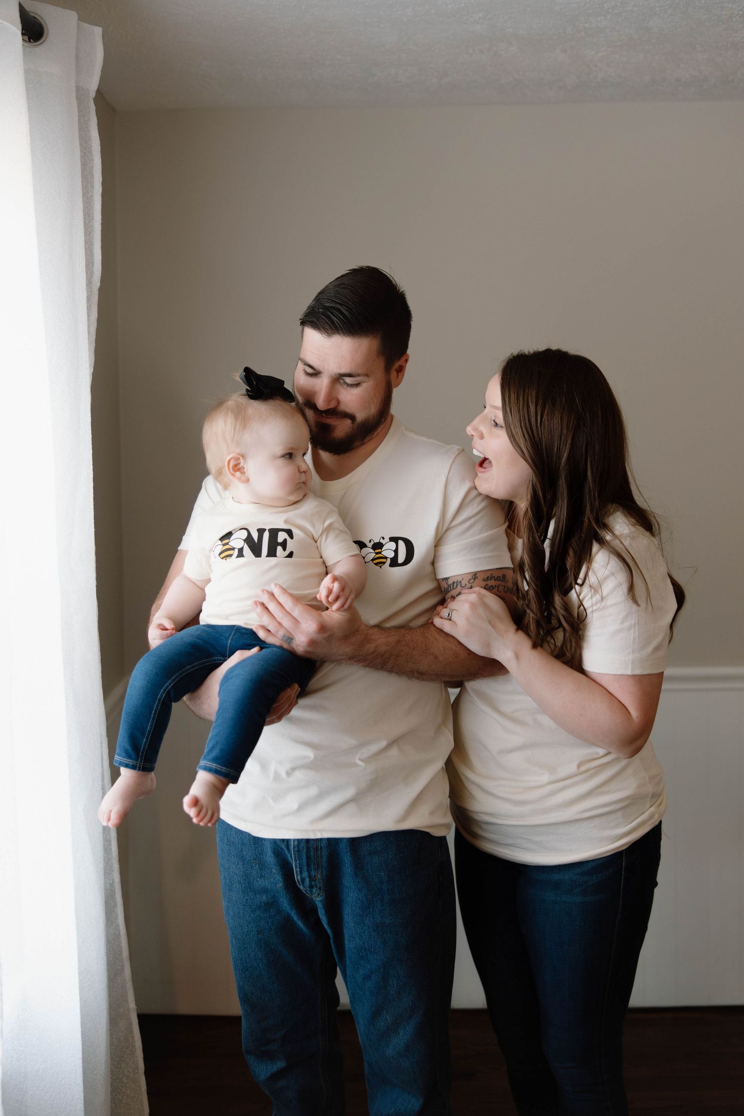 A happy family wearing matching white t-shirts shares a joyful moment together by a window.