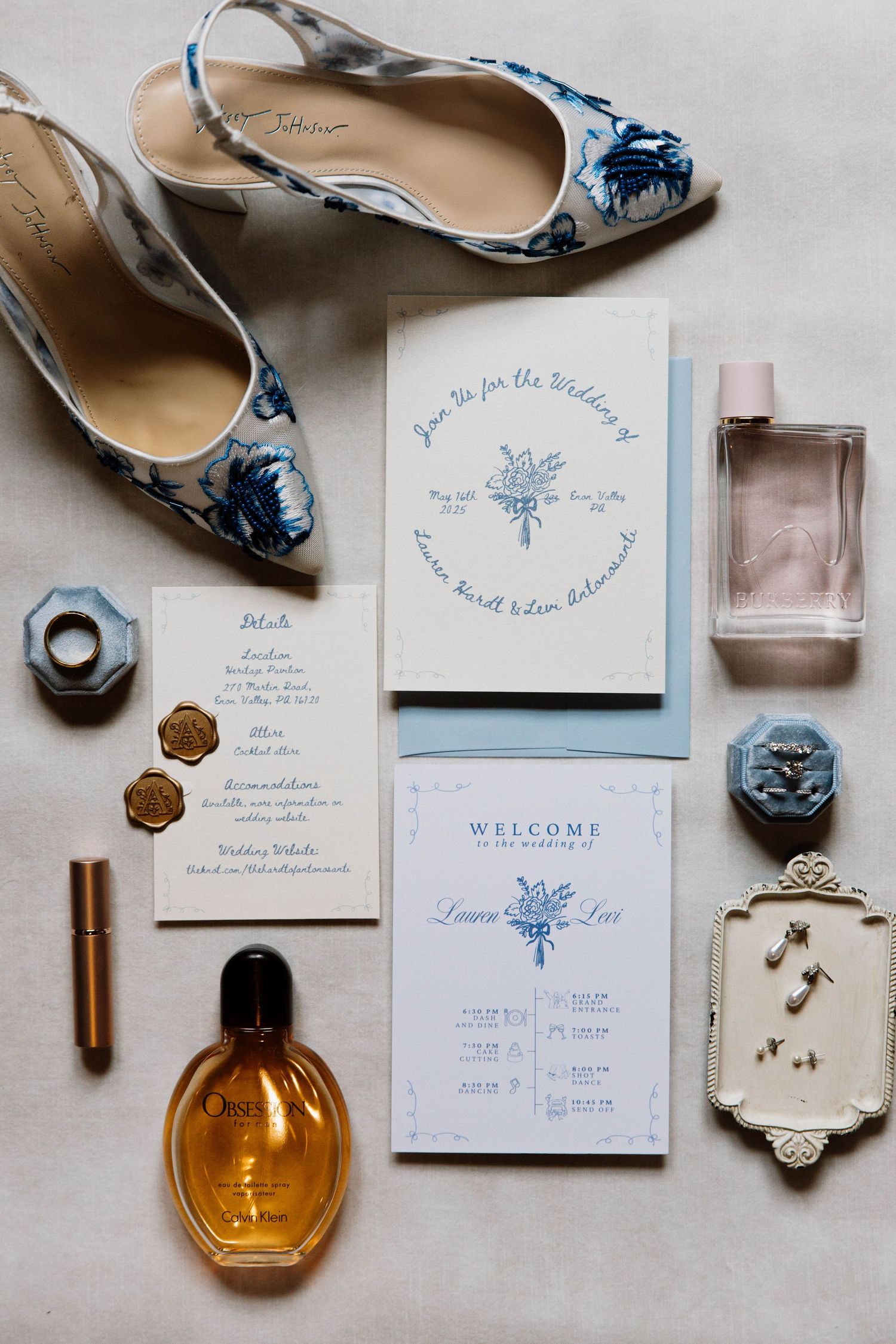 Wedding invitation suite with blue floral design laid flat with vintage perfume bottles and delicate floral heels.