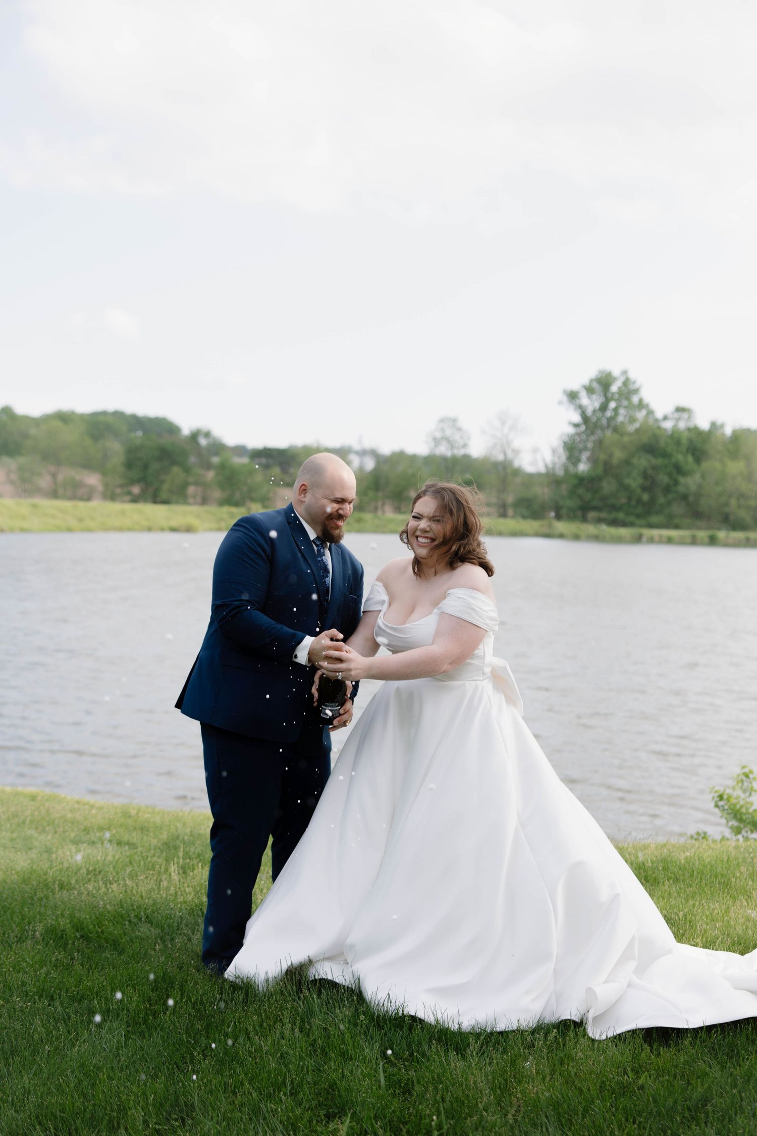 A joyful celebration of newlyweds sharing a champagne toast beside a lake on their wedding day.