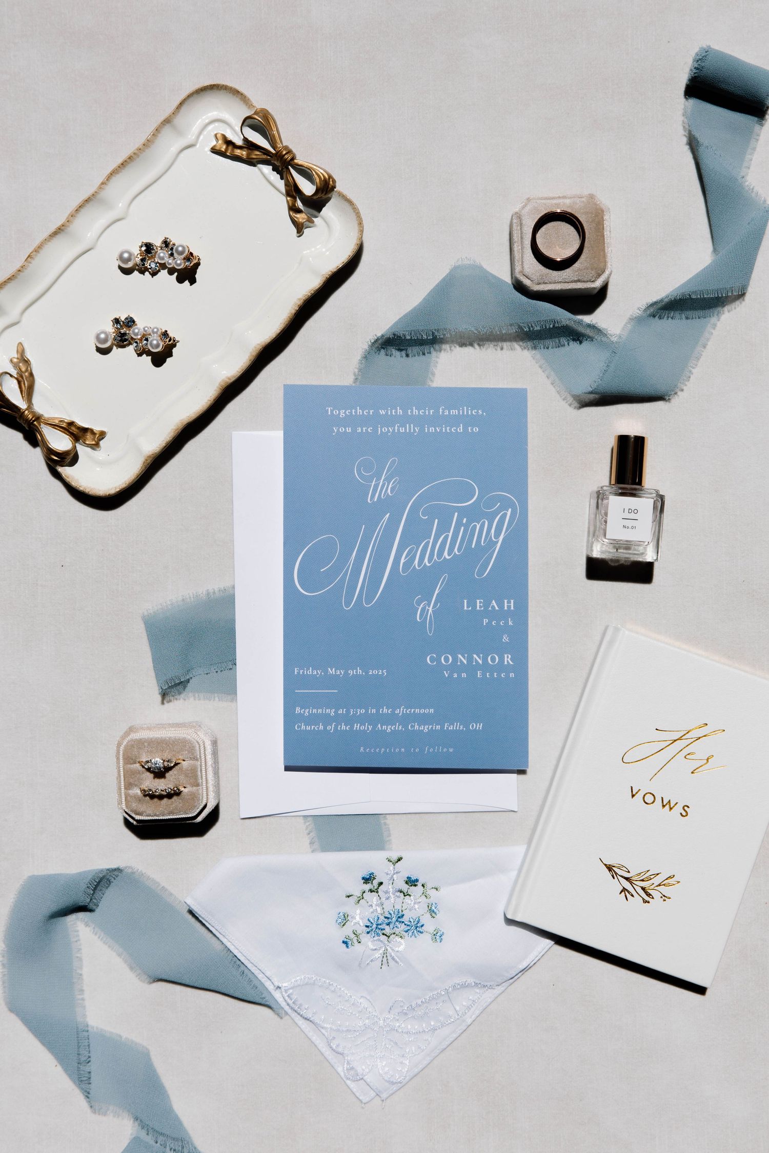 Elegant wedding invitation suite in dusty blue with silk ribbon, jewelry boxes, perfume and white embroidered handkerchief.