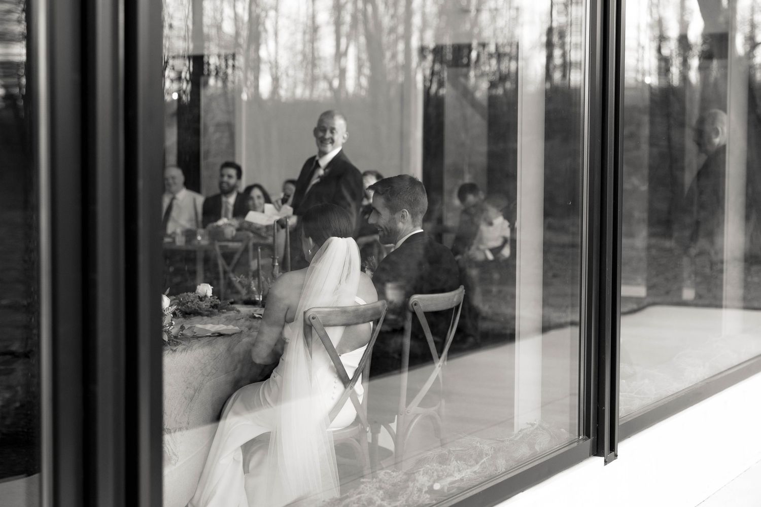 Black and white wedding reception scene viewed through reflective glass windows.