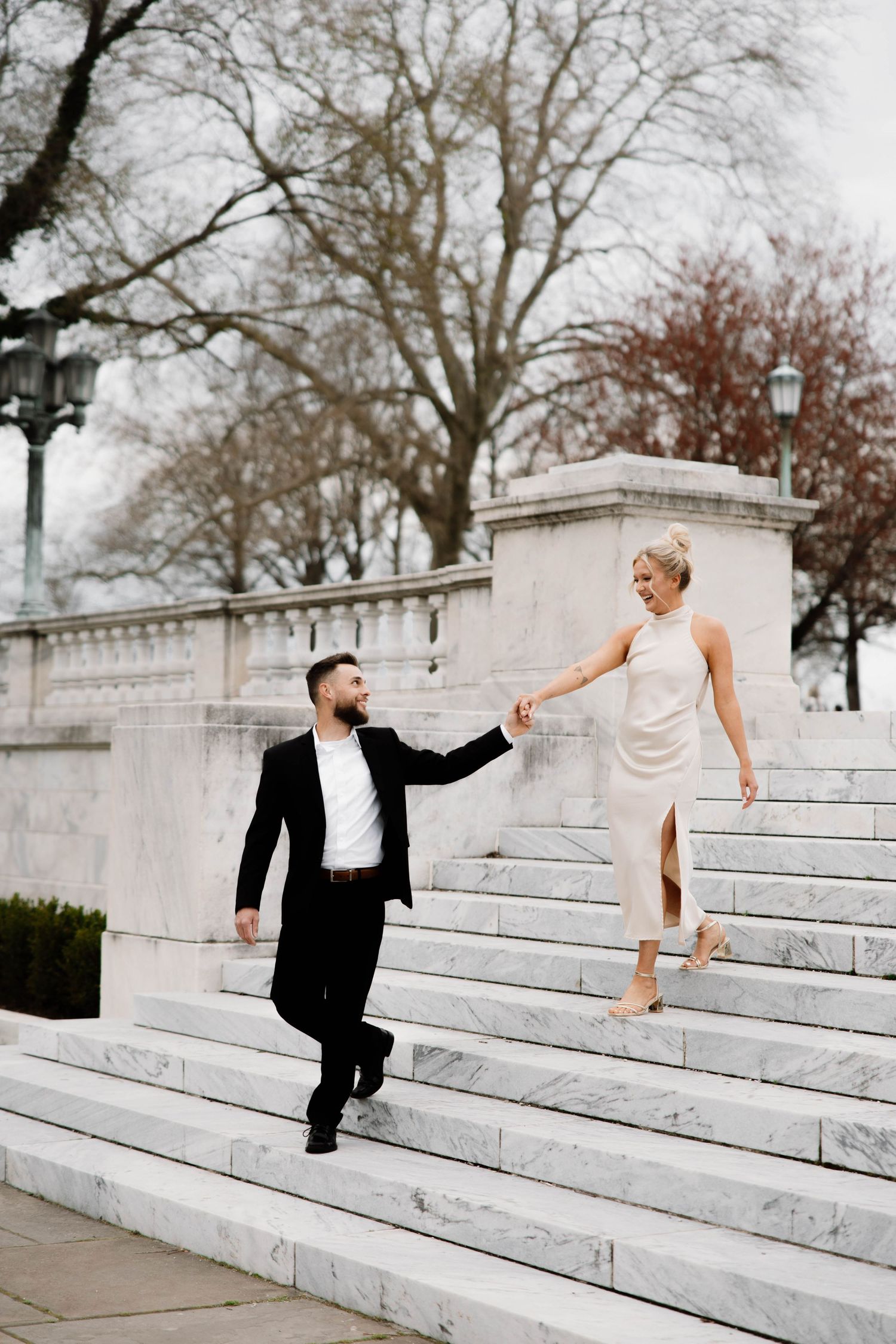 Playful formal couple holds hands while descending white stone steps outdoors. Cleveland, OH