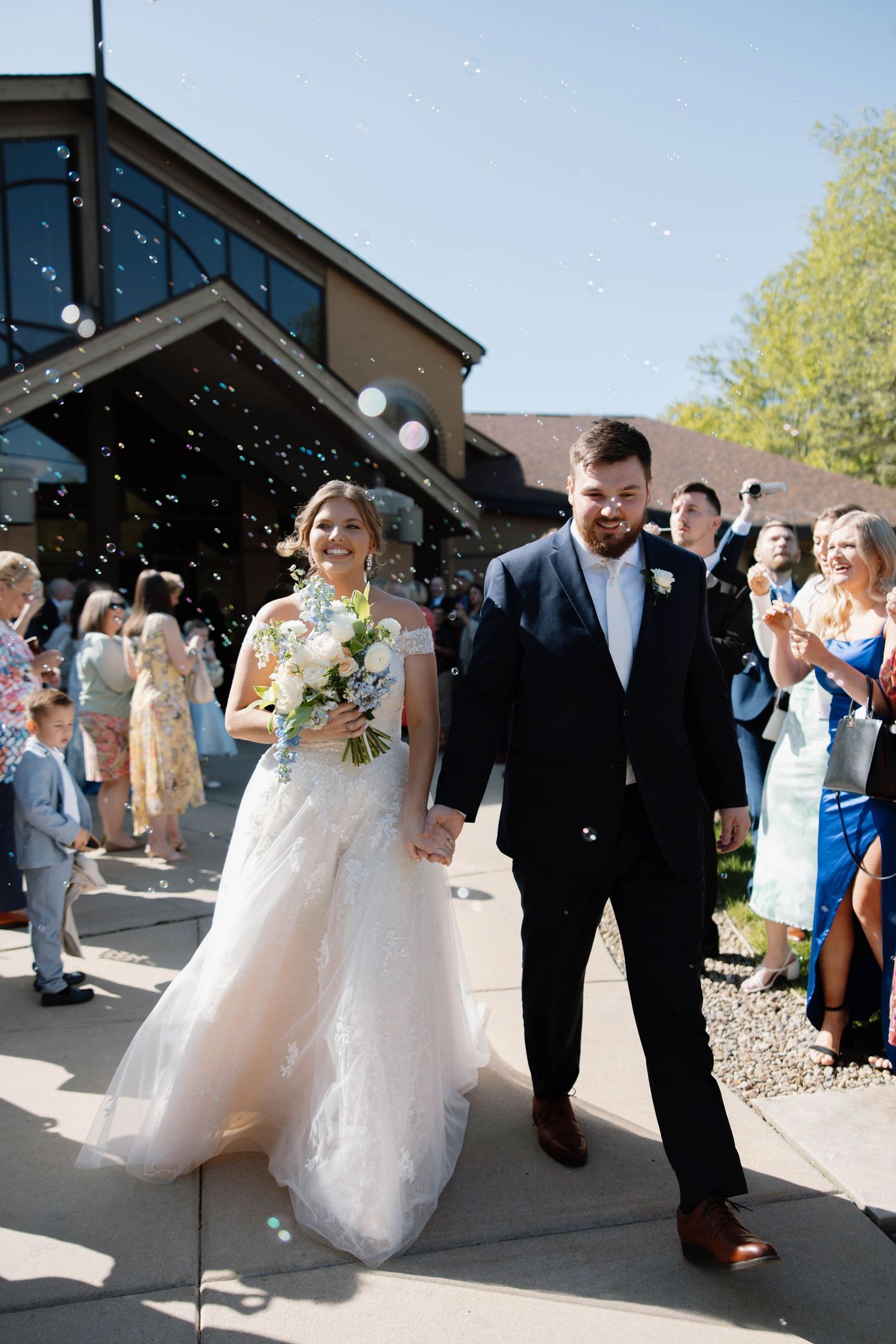 A couple exits their wedding ceremony while guests shower them with confetti outside a modern building.