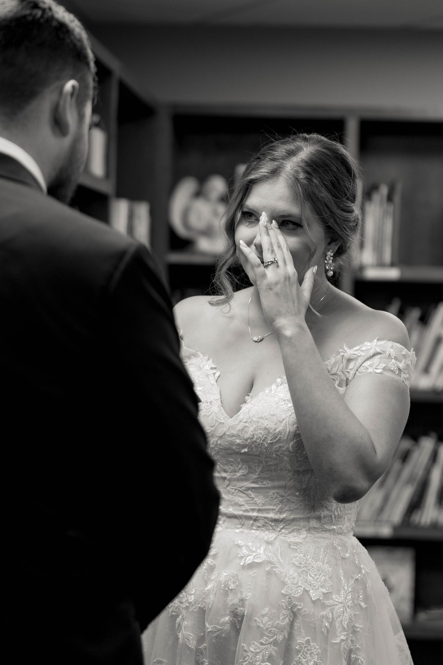 A bride in a lace wedding dress covers her mouth with emotion during an intimate moment at her wedding ceremony.