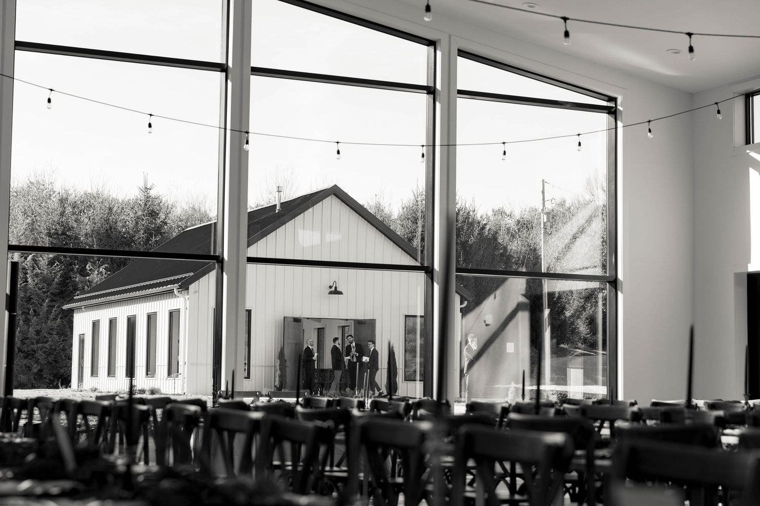 Modern reception venue with large windows and hanging string lights in black and white.