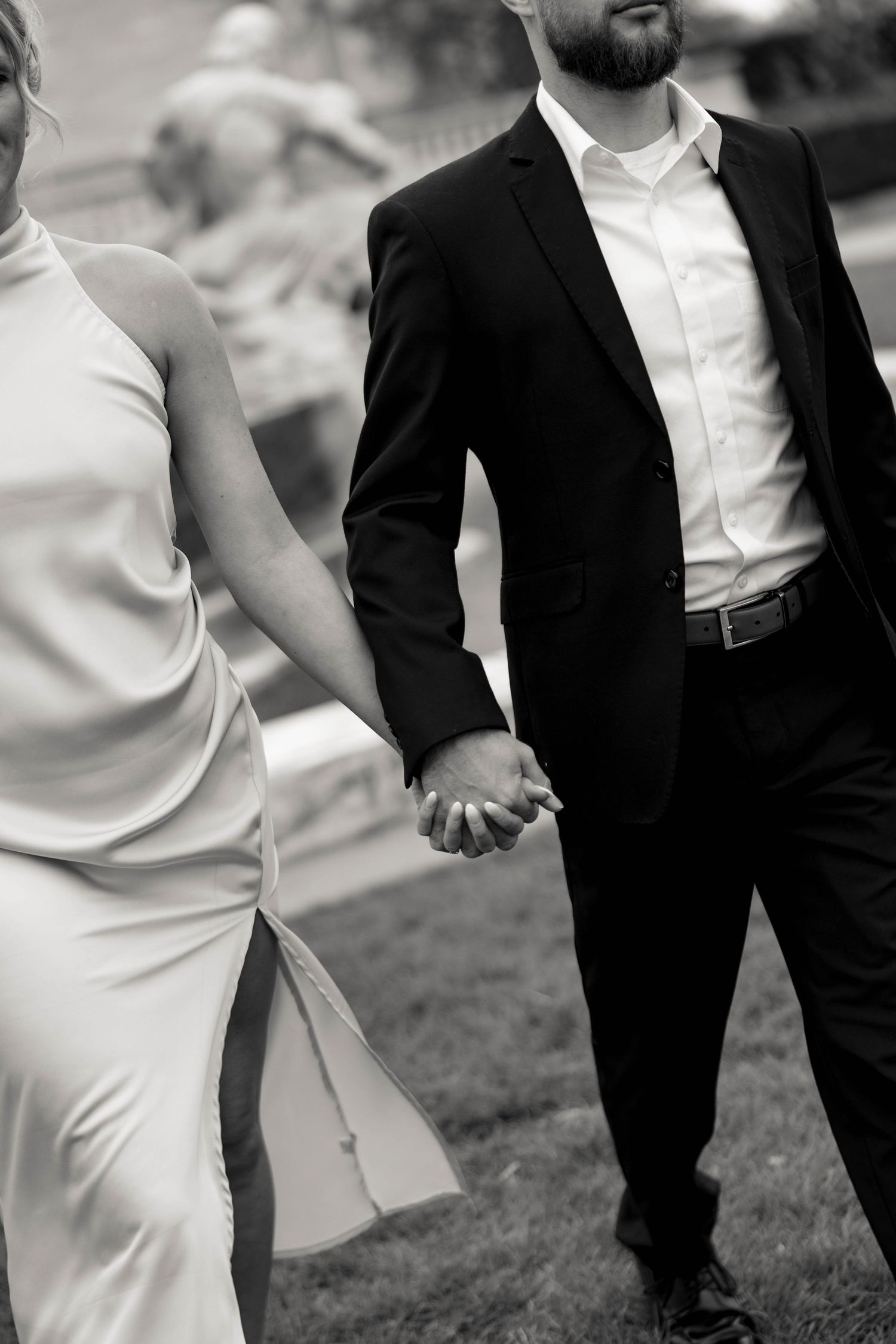 Black and white closeup of couple holding hands in formal attire against garden backdrop. Cleveland, OH