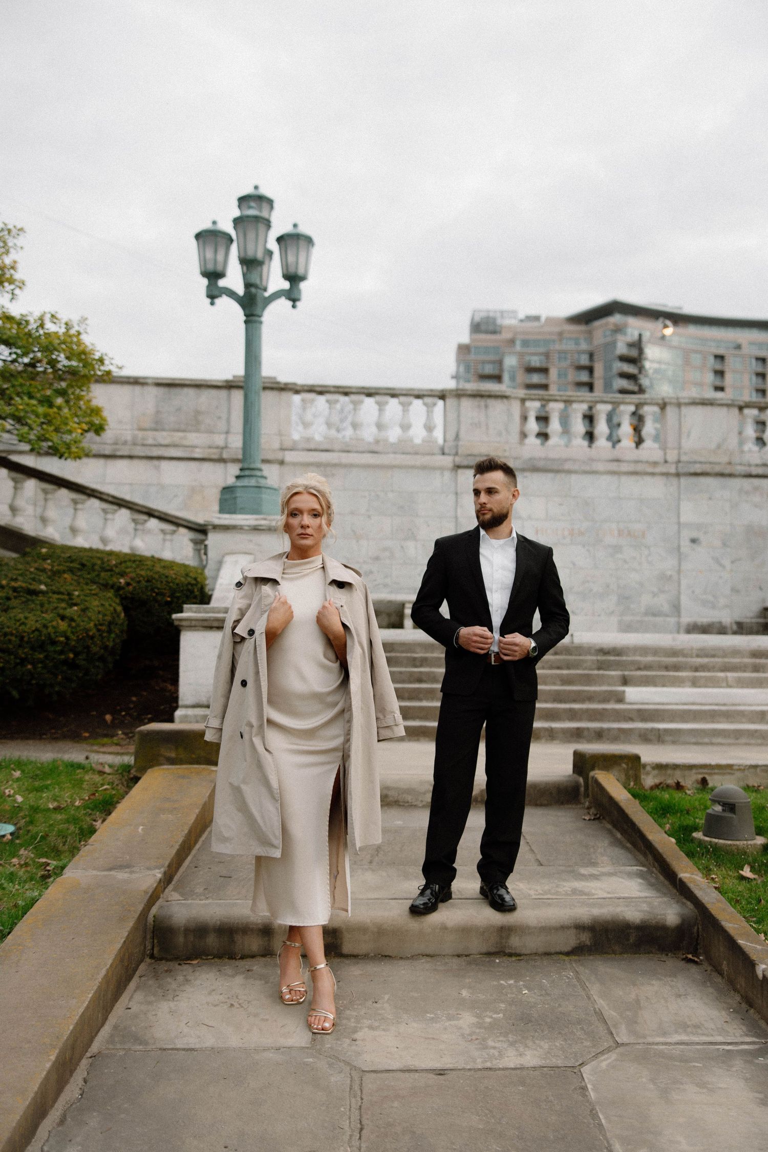 Elegant couple in formal attire poses on stone steps near vintage lamp post in classic architectural setting. Cleveland, OH