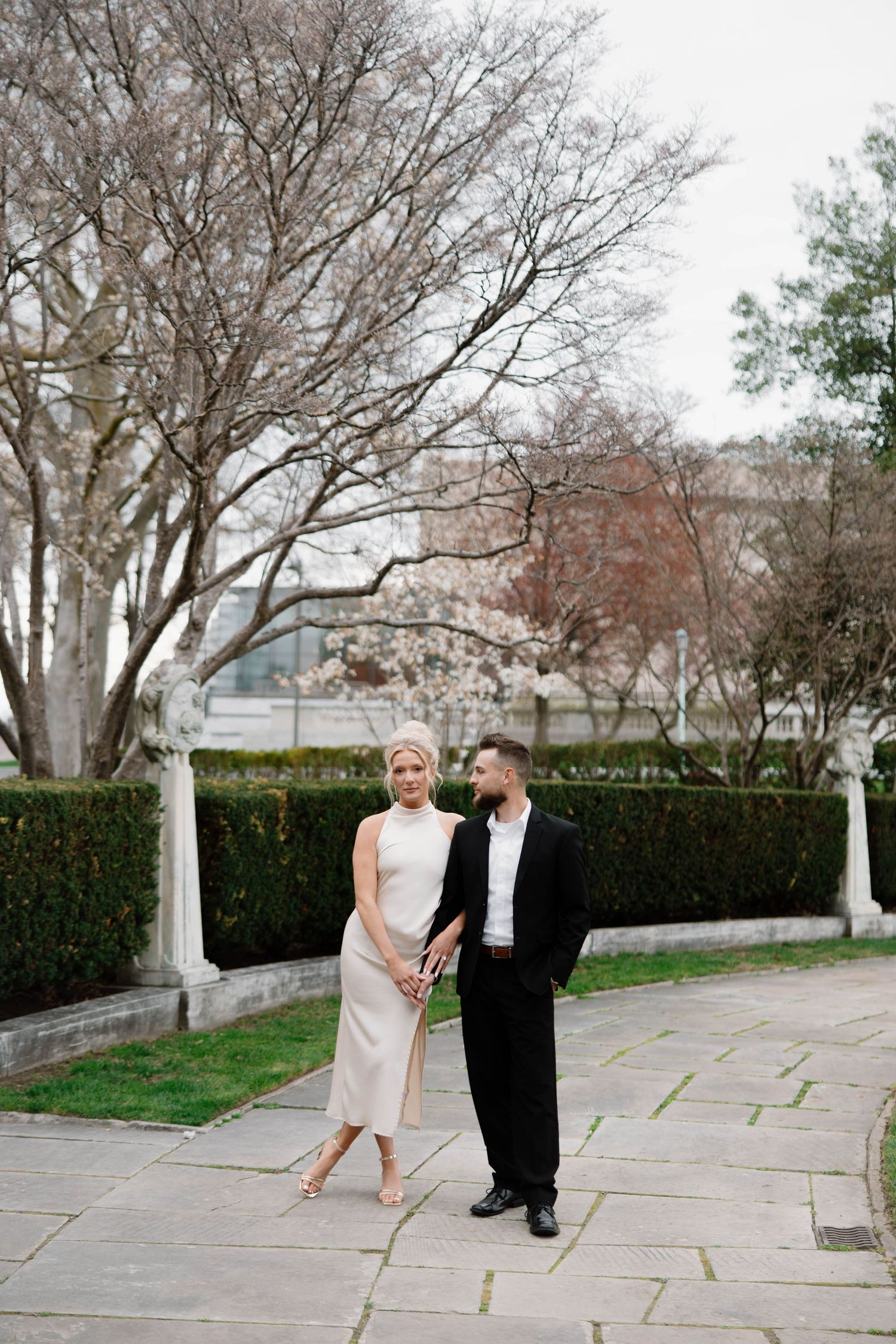 A couple in formal attire walks together on a stone path lined with trees and hedges. Cleveland, OH