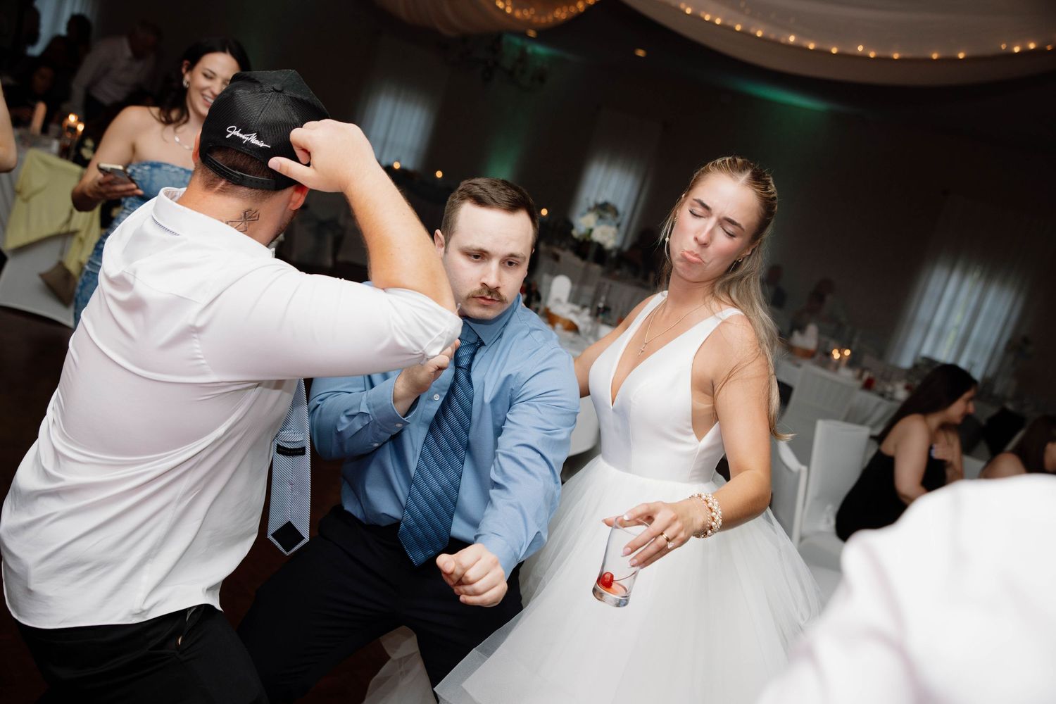 People dance together joyfully on a dimly lit dance floor at a celebration event.