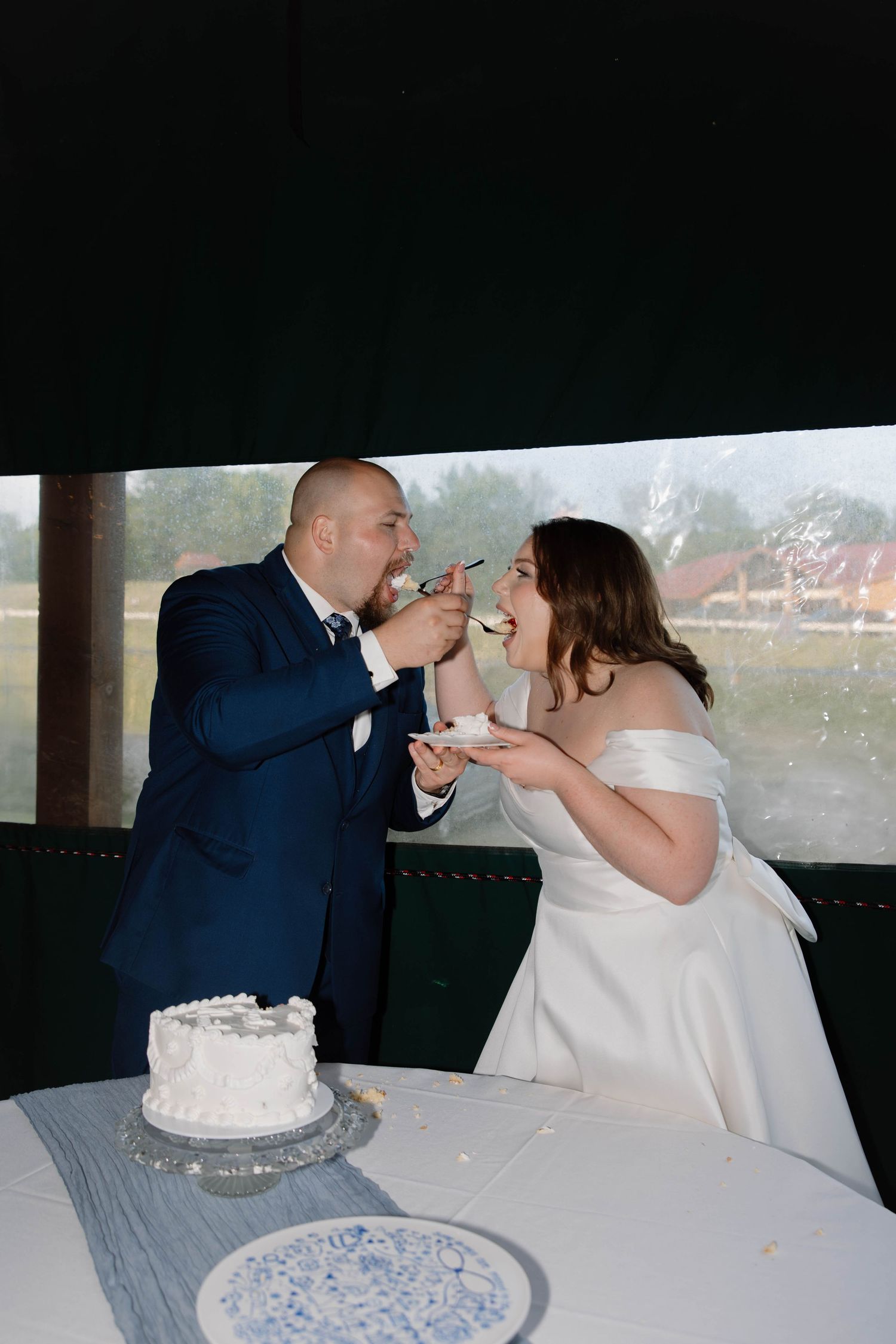Newlyweds share cake during their wedding reception while seated at a table.