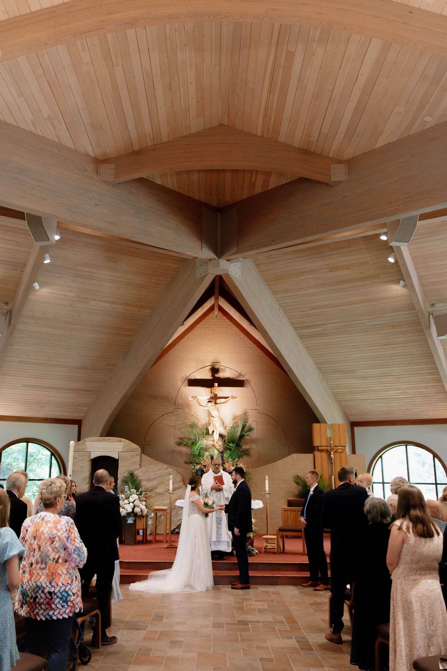 Wedding ceremony taking place in a beautiful wooden chapel with vaulted ceilings and arched windows.