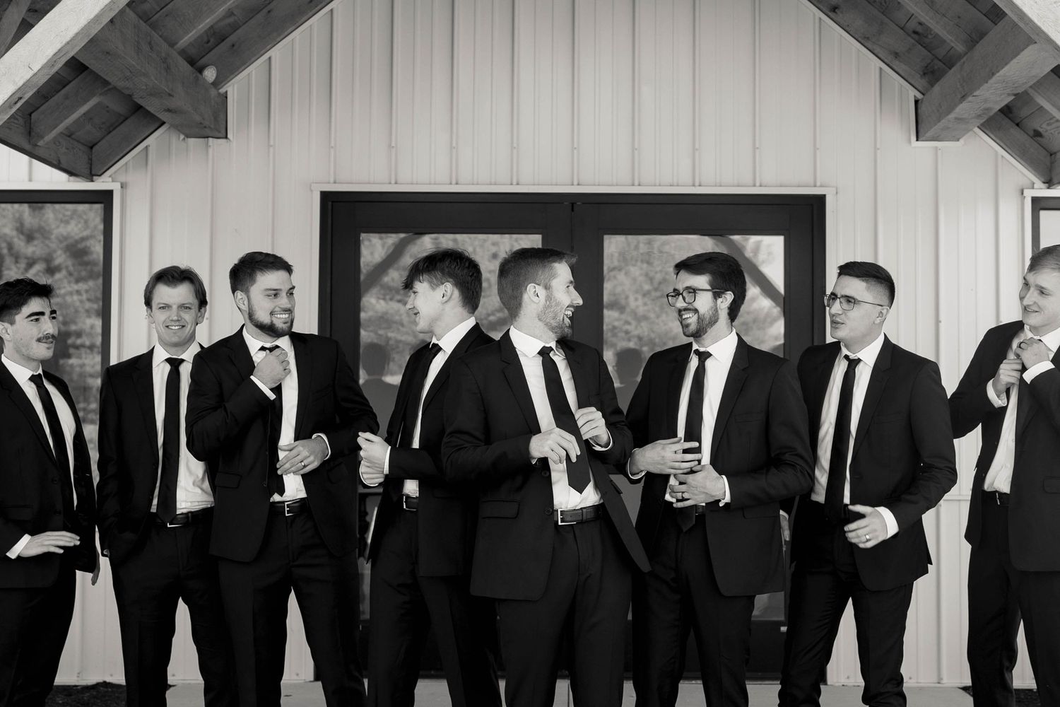 Group of groomsmen in black suits sharing laughs during wedding preparations.
