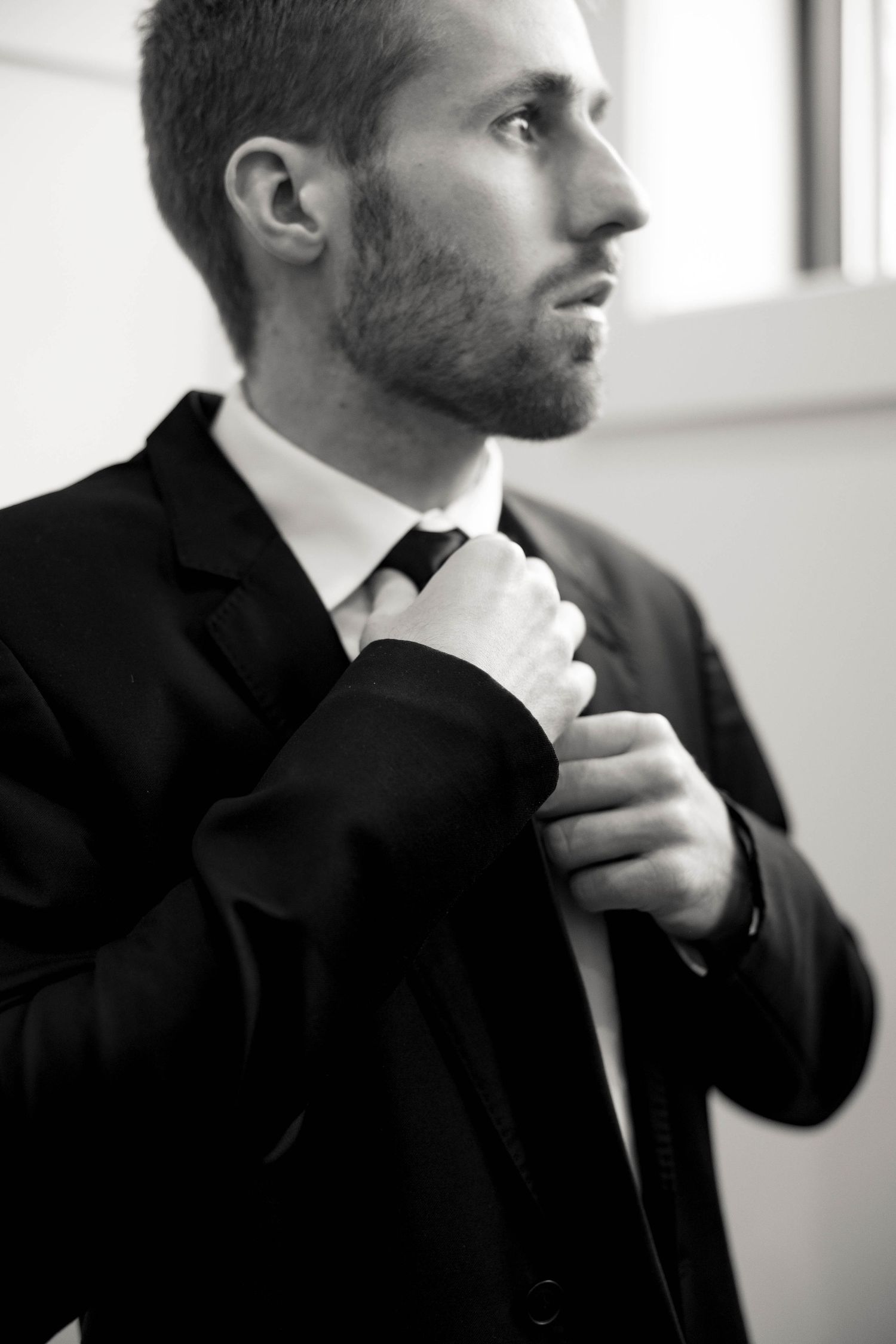 Black and white portrait of a man adjusting his tie while wearing a formal suit.