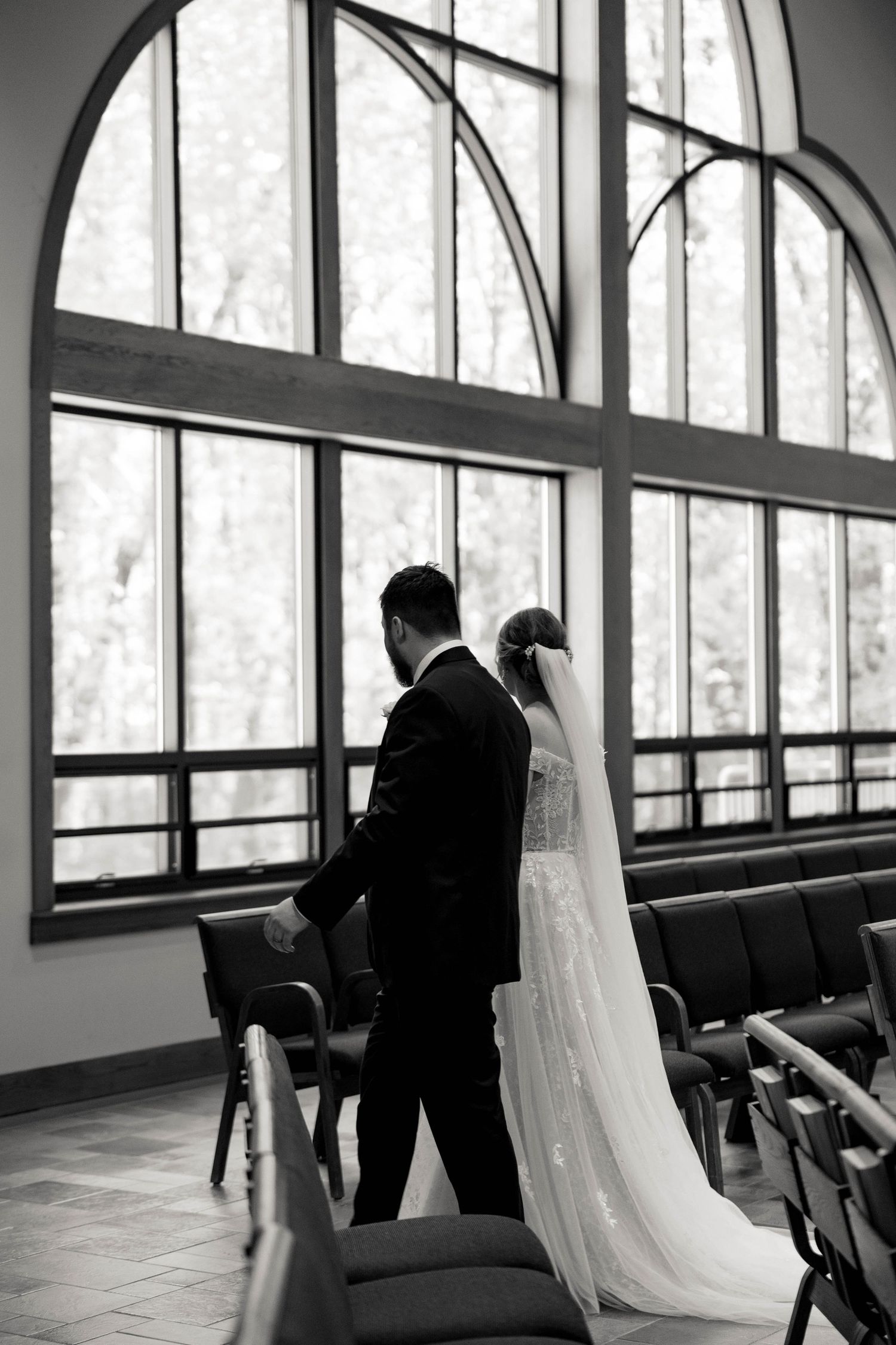 A silhouette of a couple during their wedding ceremony standing in front of large arched windows in black and white.