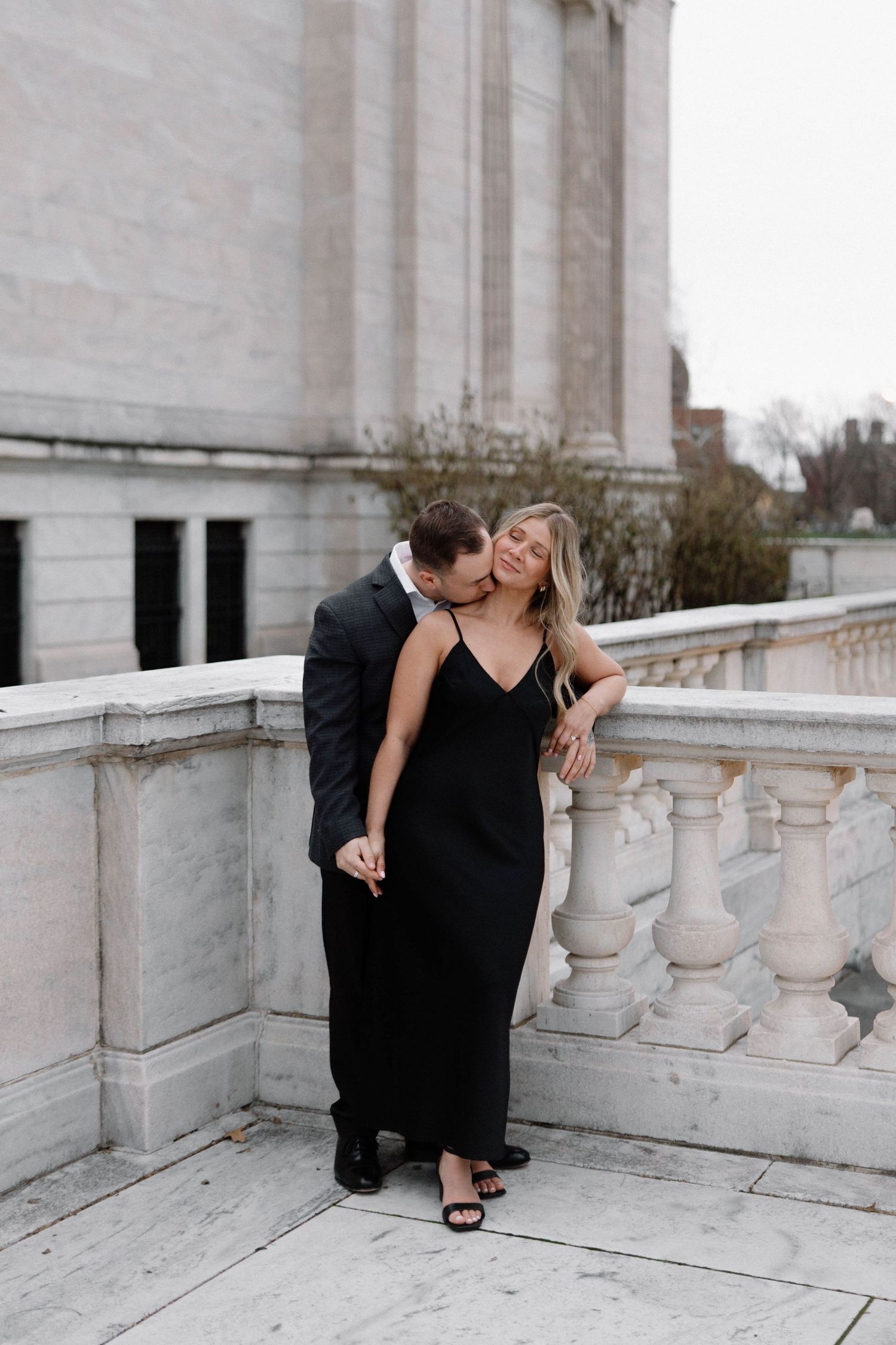 Couple shares intimate moment on marble balcony in formal black attire. Cleveland, OH