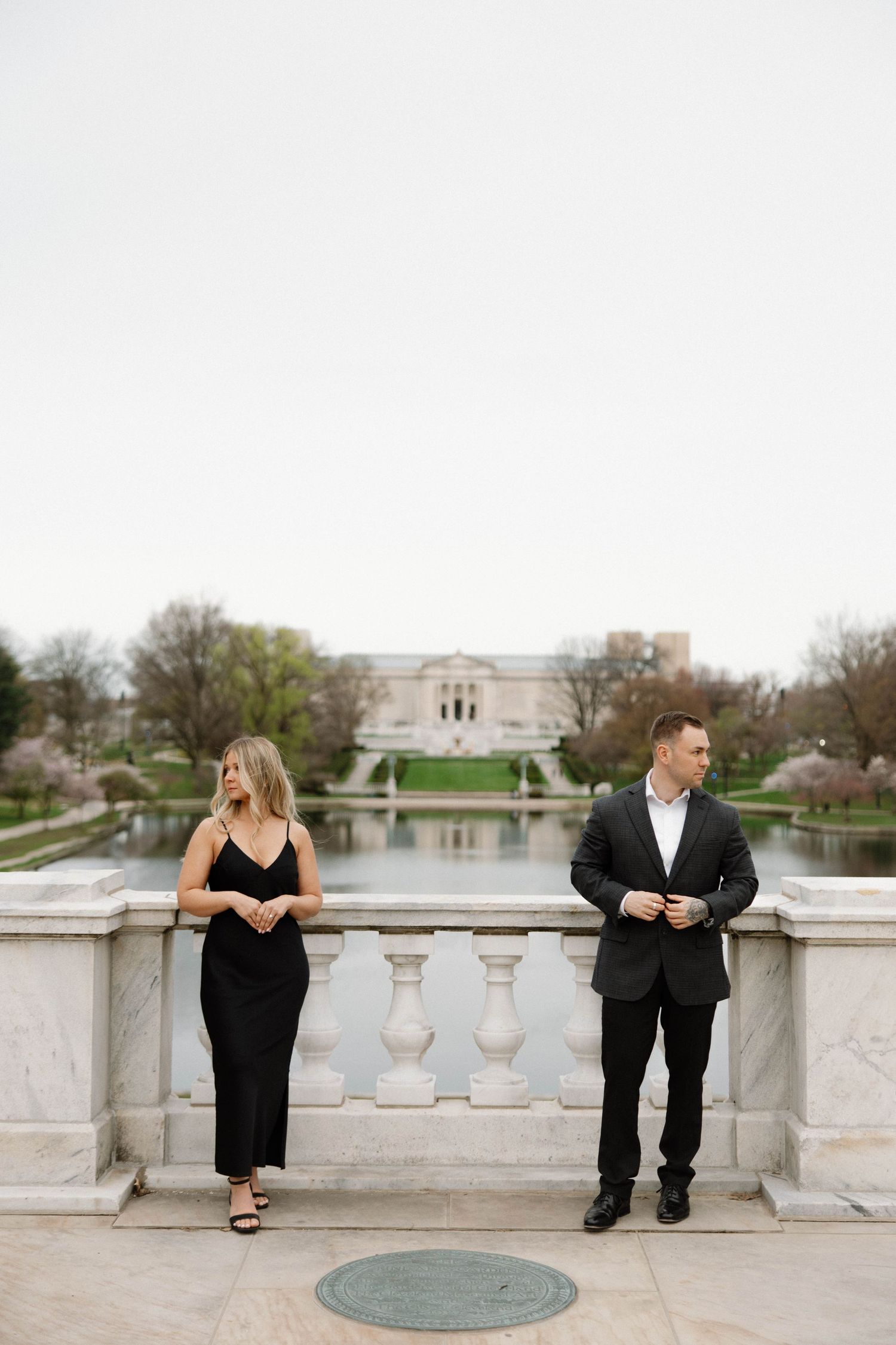 Couple in formal attire poses separately on marble balcony with scenic backdrop. Cleveland, OH
