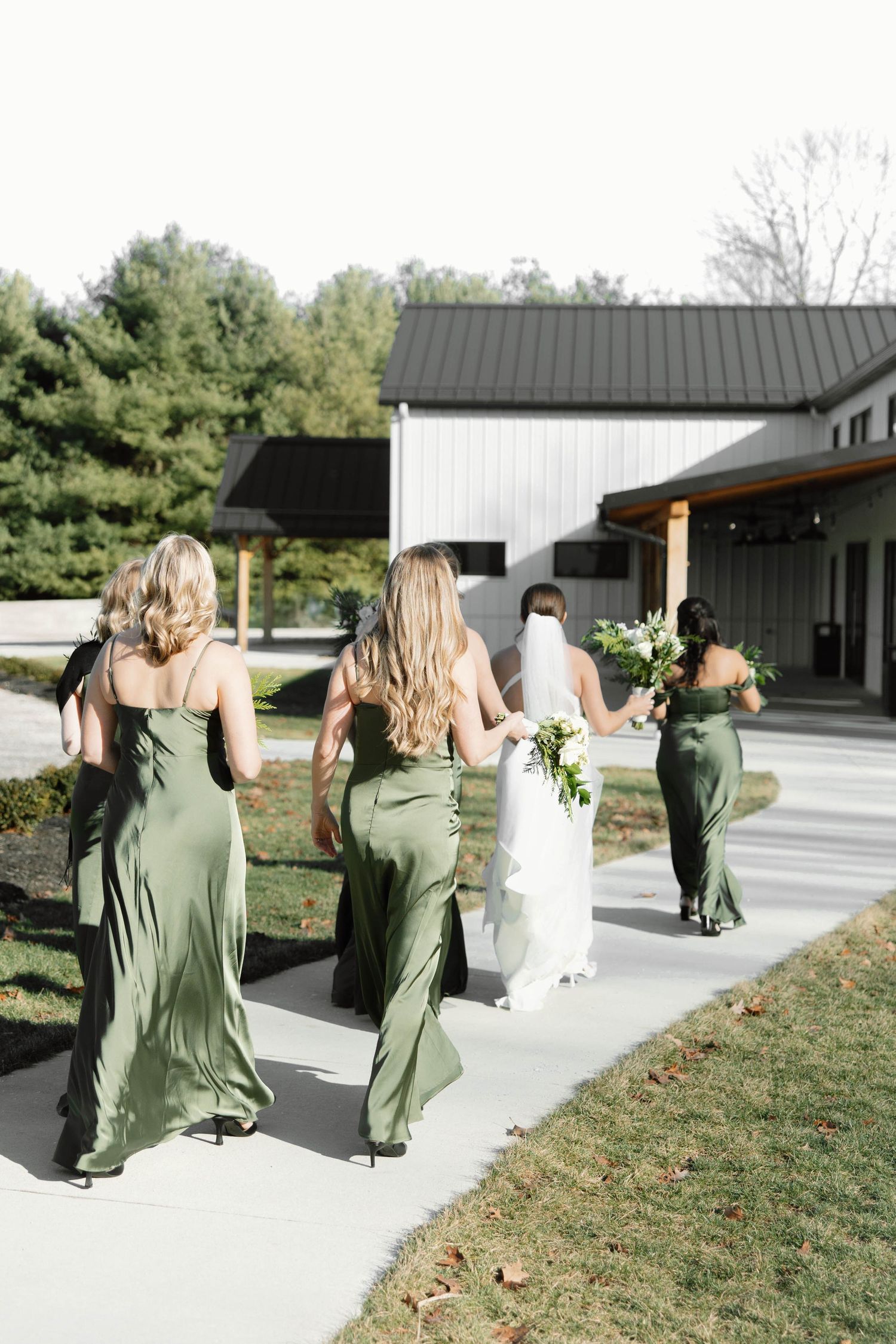 Wedding party in sage green dresses walking along a modern white building pathway.
