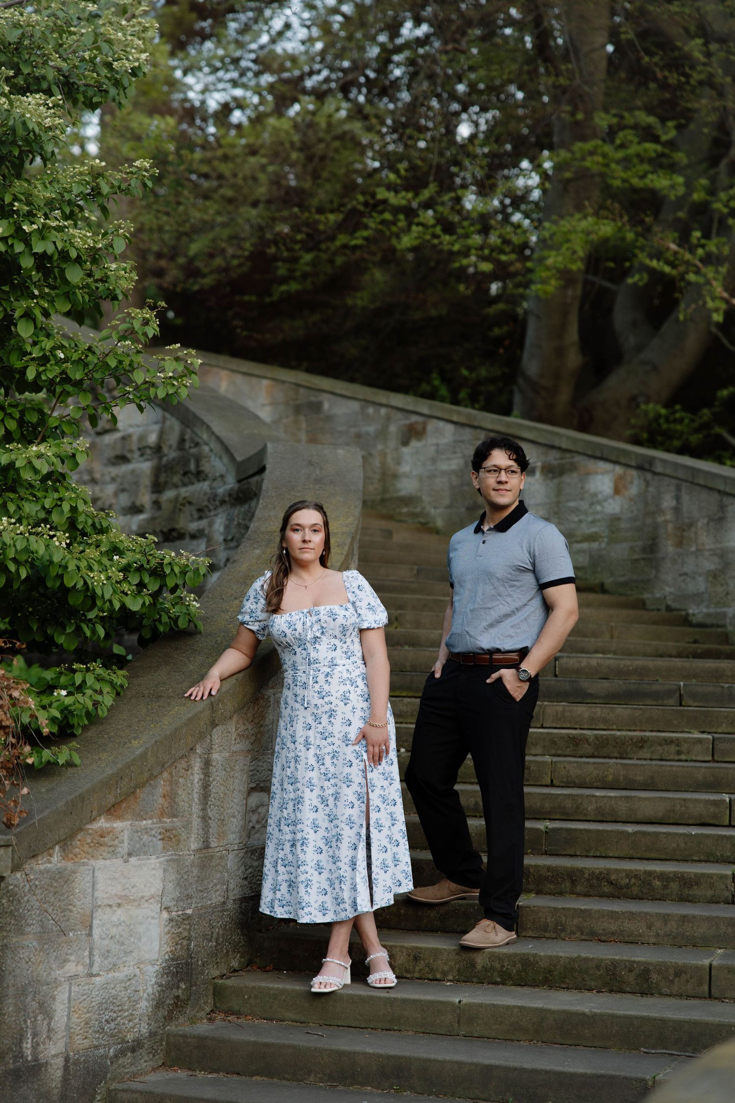 A couple poses together on stone garden steps surrounded by lush greenery in an elegant outdoor photo shoot.