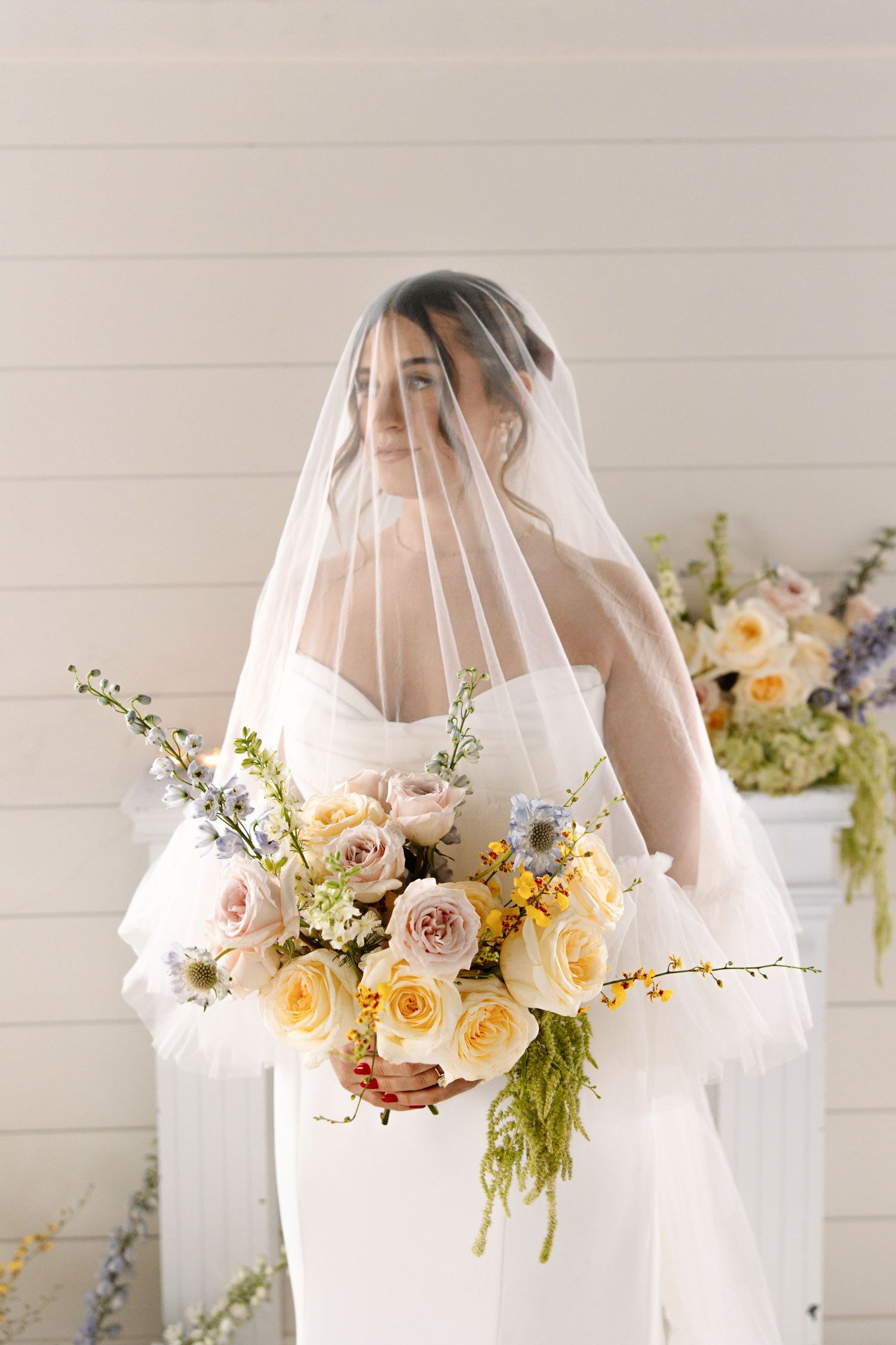 Elegant bridal portrait with sheer veil and lush bouquet of pink and yellow roses against white wall. Cleveland, OH