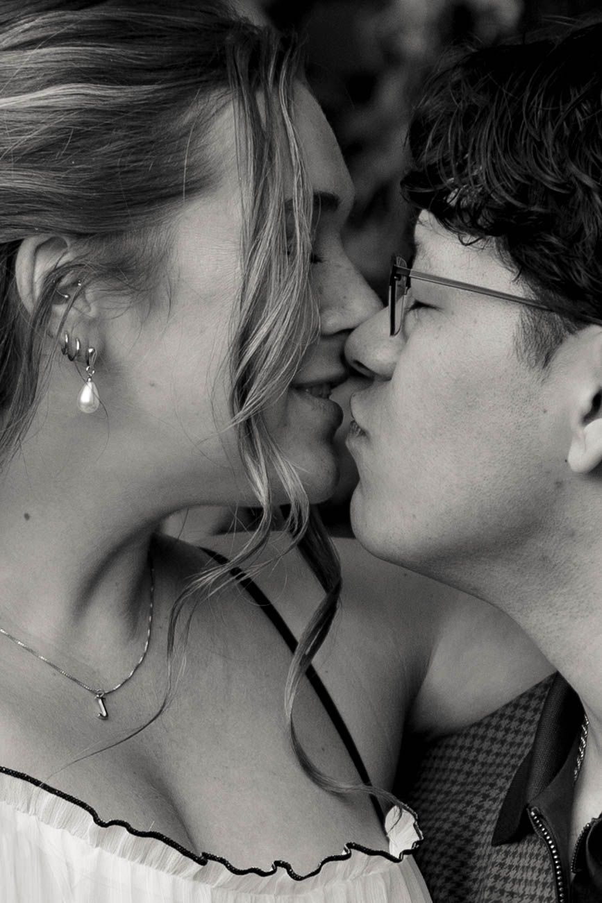 Black and white romantic close-up shot of a tender kiss, with a visible pearl drop earring and soft curled hair.