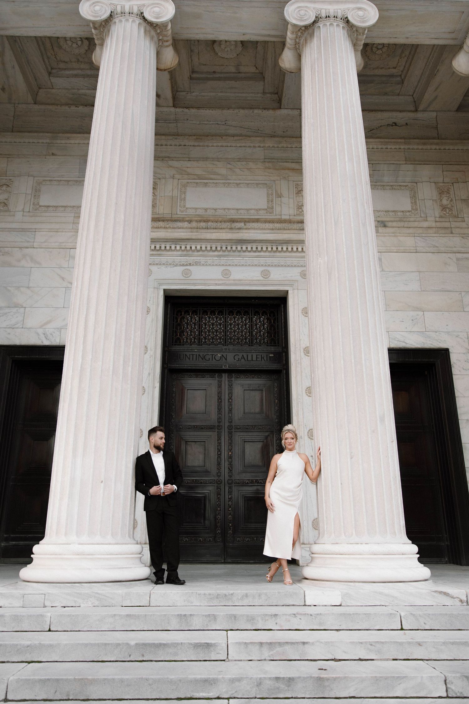 Stylish duo poses between grand white marble columns at historic building entrance. Cleveland, OH