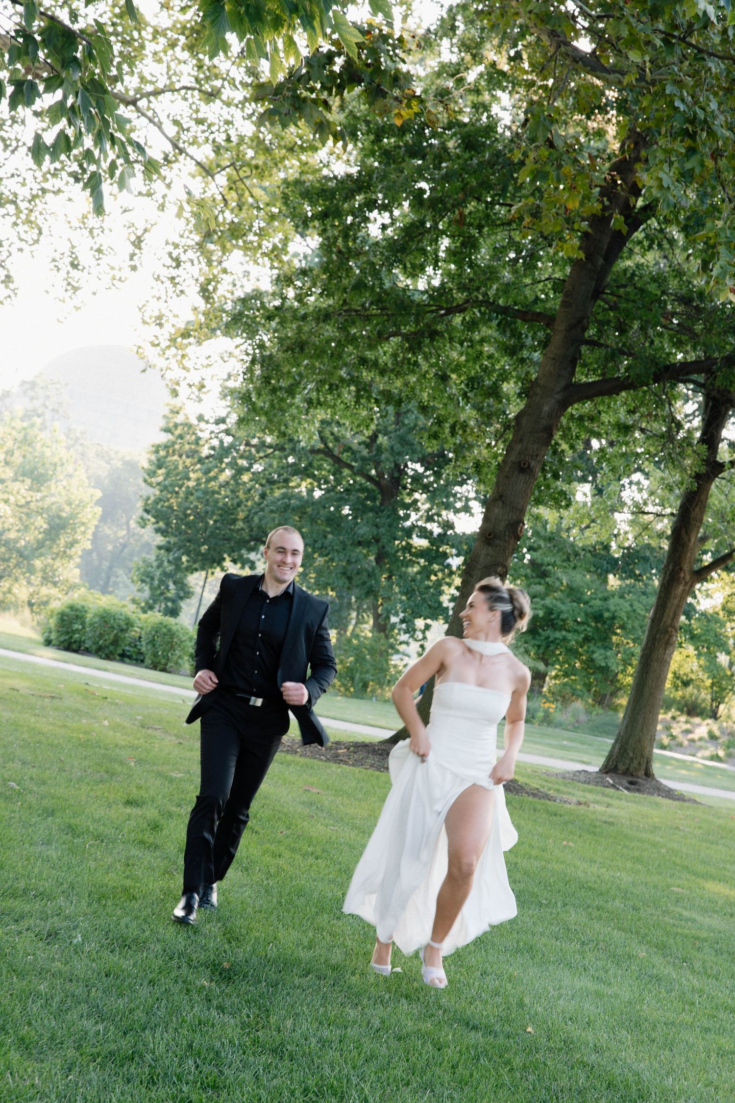 A couple enjoying a playful and candid moment running together on a grassy slope surrounded by trees.